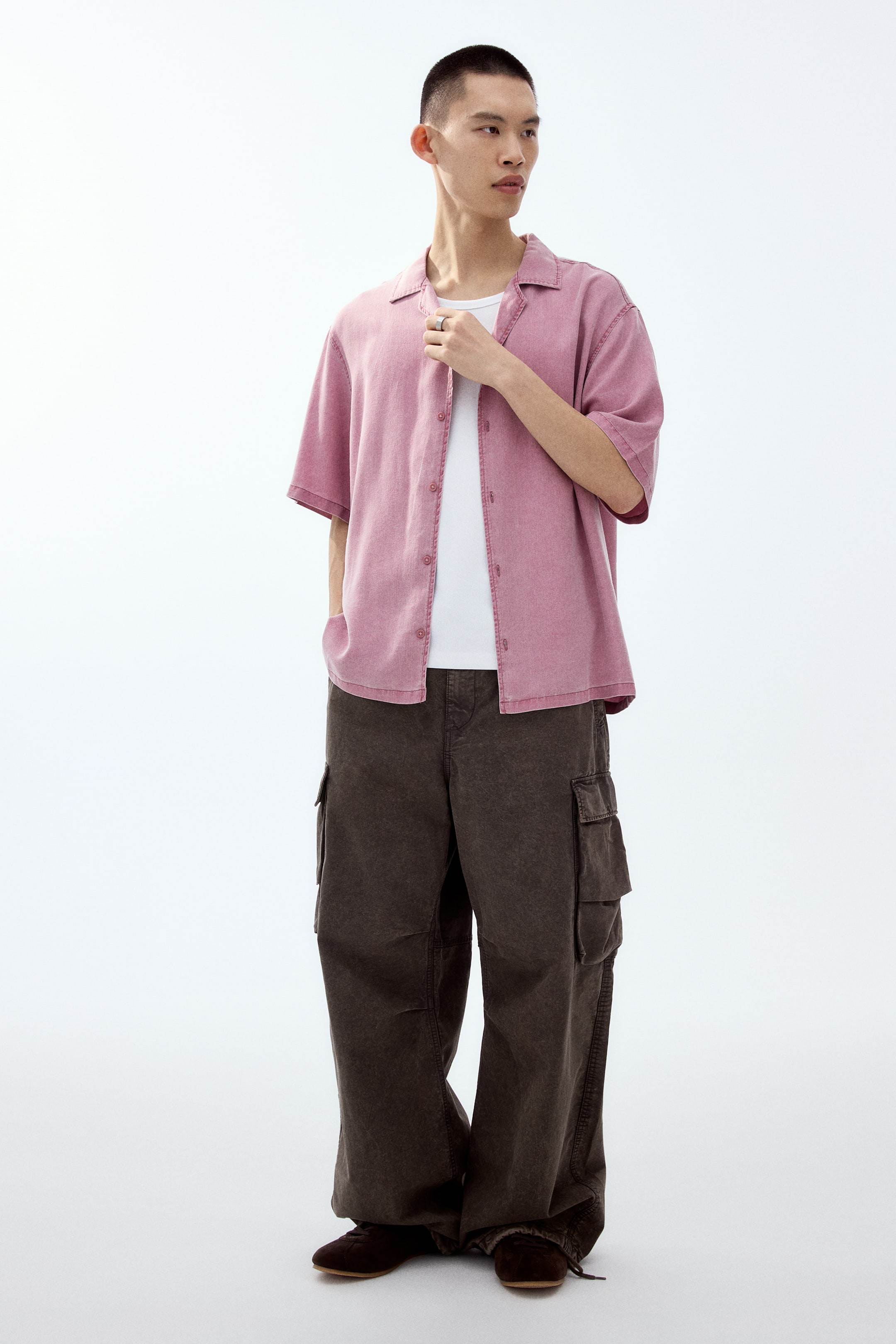 View larger image: Dark brown cargo pants showcase a loose, wide-leg fit, viewed from the front at a slight angle to the right. They feature large flap cargo pockets on the sides of the thighs and are designed to pool slightly at the ankles.