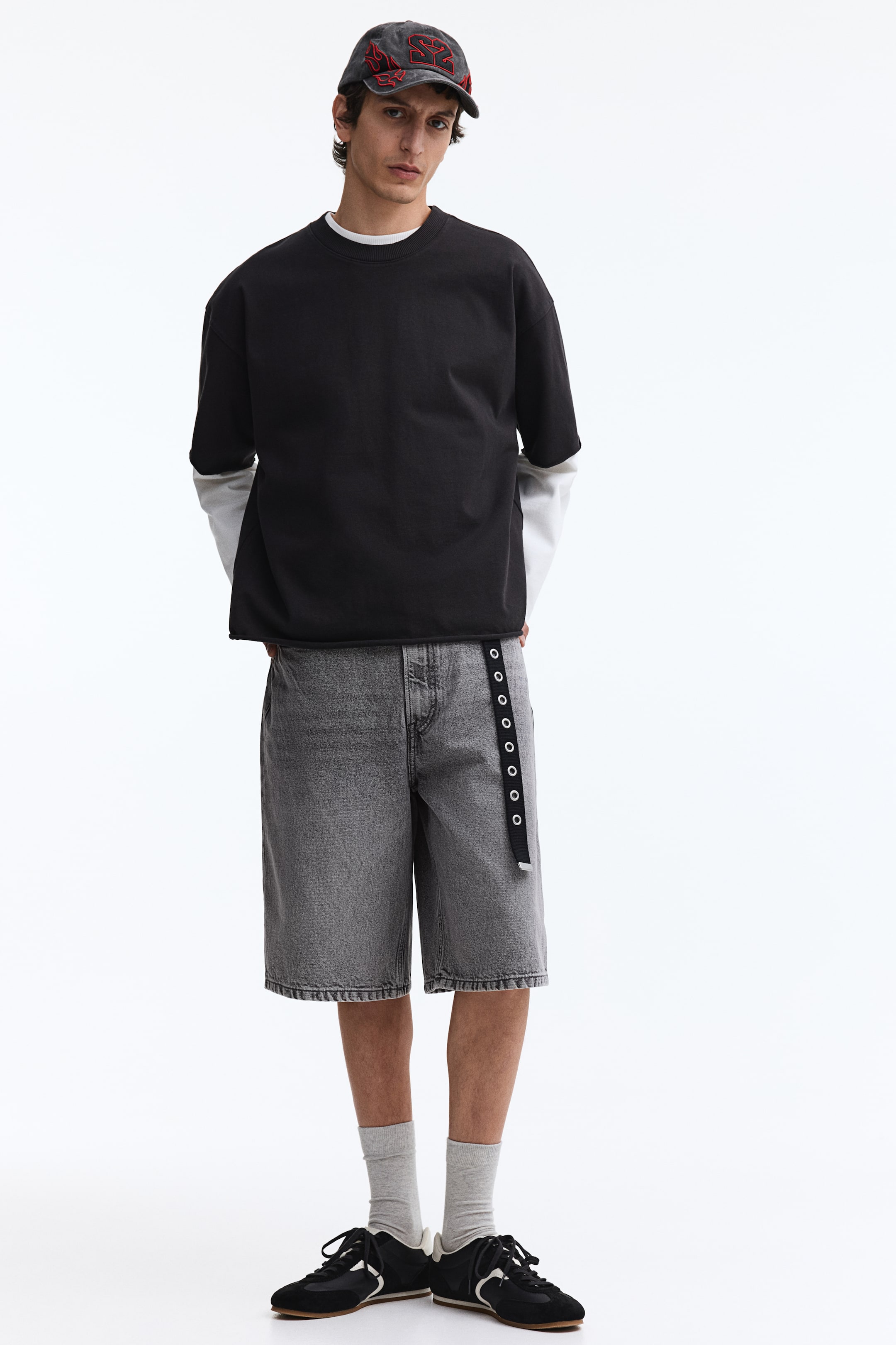 View larger image: The black oversized short-sleeve t-shirt features a crew neck and raw hem. It is styled with its short sleeves over a white long-sleeve shirt, facing forward.