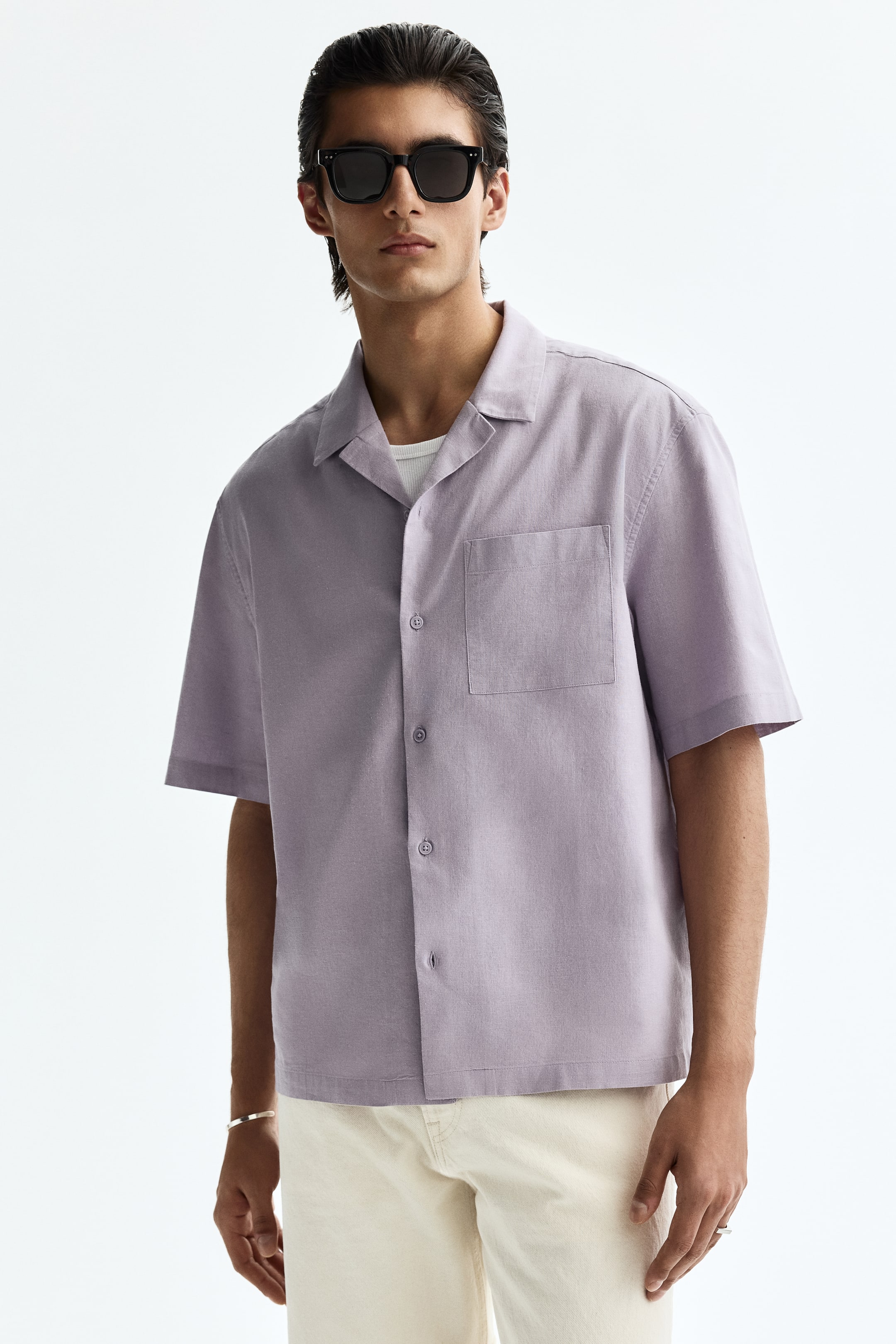 View larger image: A lilac short-sleeved shirt features a camp collar and a button-front closure, with a single patch pocket on the left chest. It is positioned front-facing and angled slightly to the right, showcasing a white undershirt beneath the open collar.