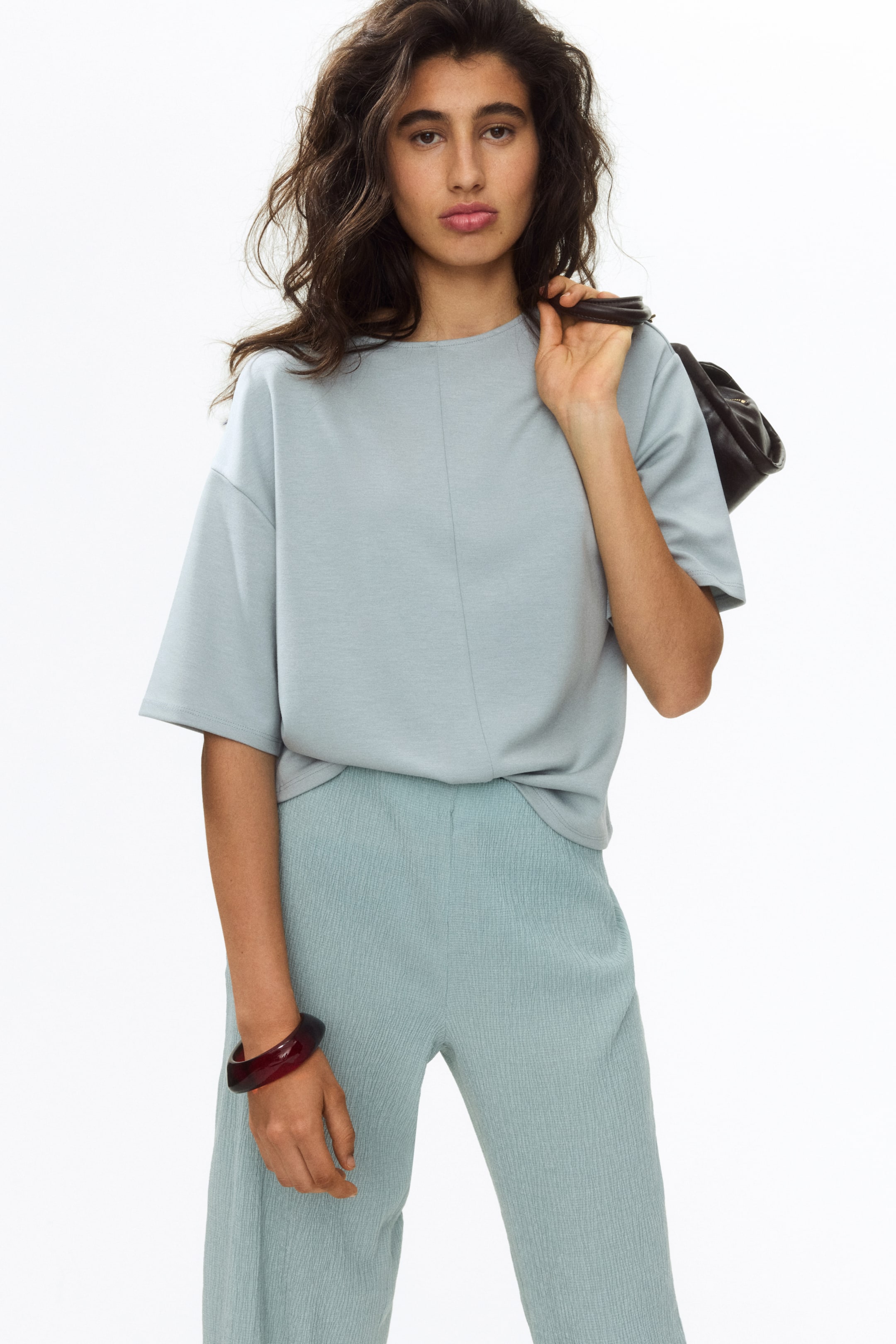 View larger image: A pale blue short-sleeved top featuring a round neck and a visible central vertical seam, offering a relaxed fit. It is styled with matching pale blue textured trousers, which showcase a crinkled fabric and a relaxed, wide-leg cut. The top is partially tucked into the front of the trousers.
