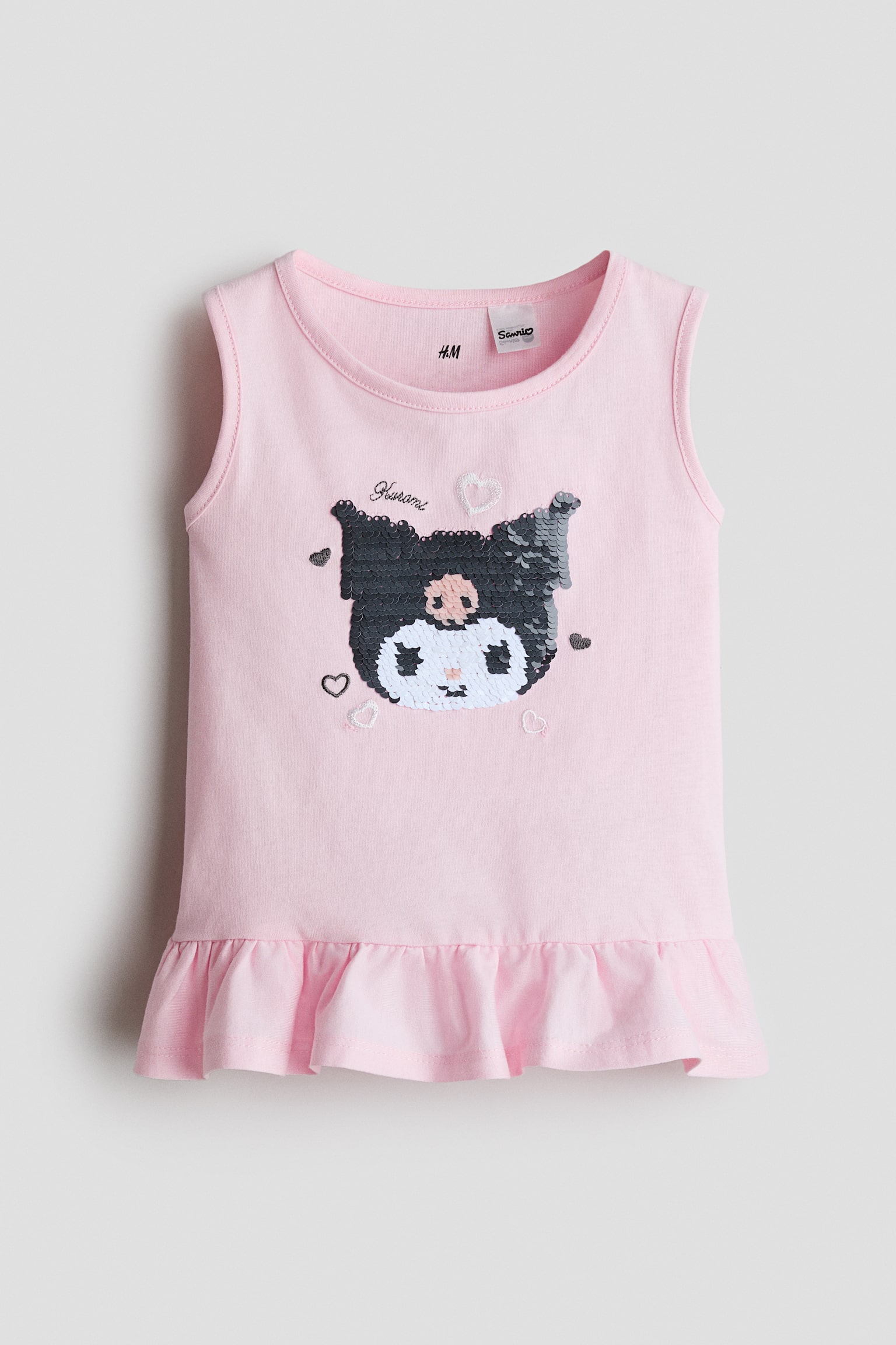 A light pink sleeveless top in soft cotton jersey is shown from the front, featuring a round neckline and a wide, flared frill trim at the hem. A sequined Kuromi character motif decorates the centre front, surrounded by small embroidered hearts. - 1