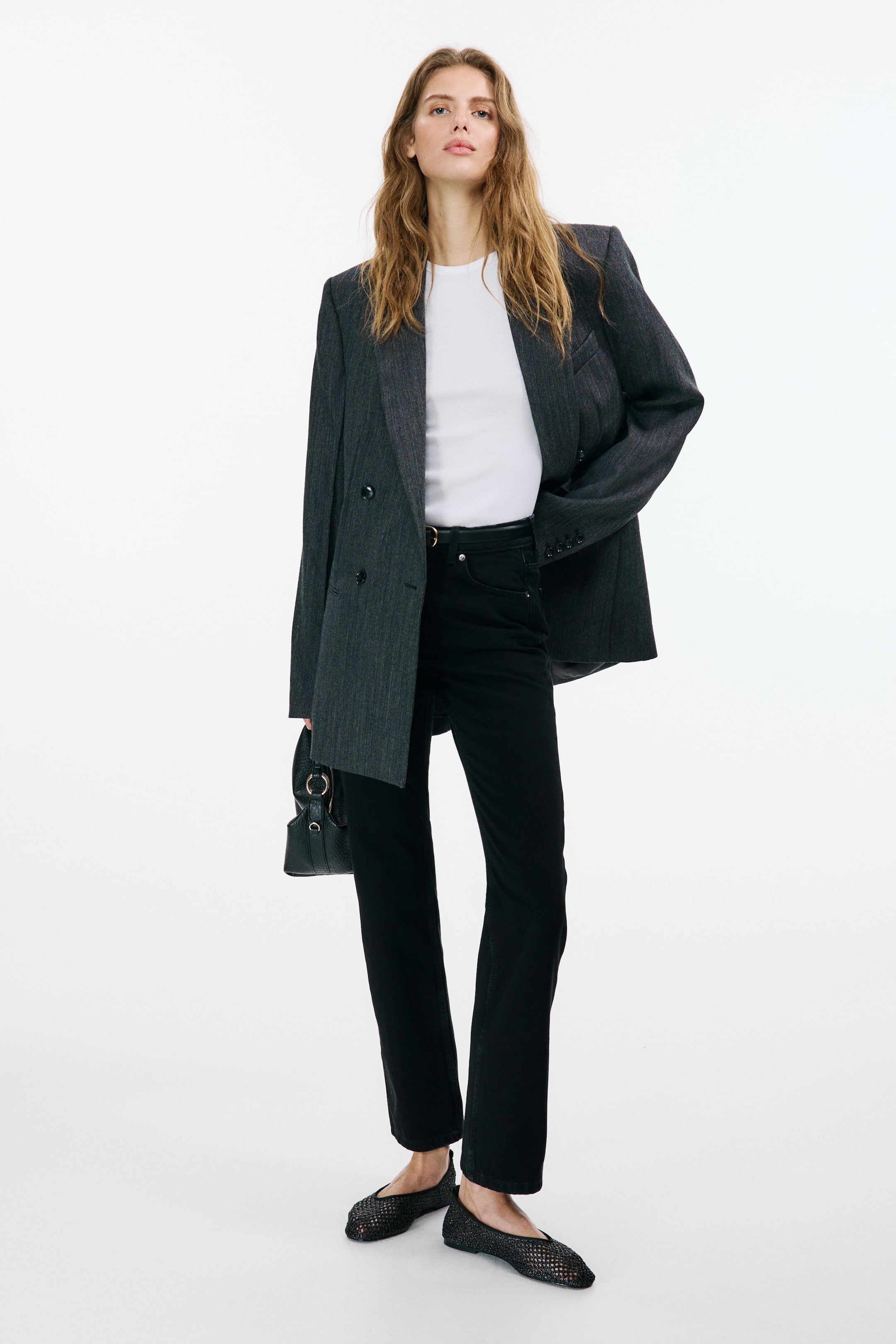 Agrandir l'image: Un t-shirt blanc ajusté en jersey côtelé de coton avec une bordure étroite autour de l'encolure est porté par le mannequin. Il est superposé sous un blazer gris foncé et rentré dans un jean noir.