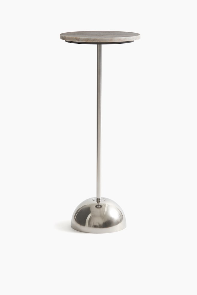 A pedestal presents a round marble slab at its top. A slender metal column supports the slab and connects to a dome-shaped, reflective metal base. - 1