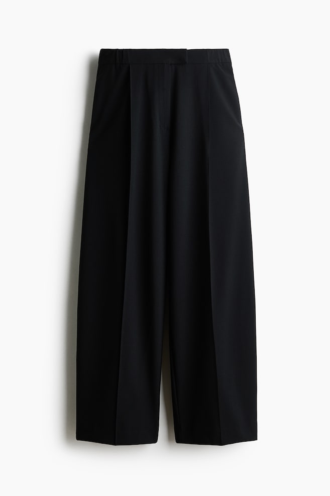 Diese schwarzen, locker geschnittenen Hosen aus Webstoff hÃ¤ngen in einer Vorderansicht und zeigen ihre weite Barrel-Leg-Silhouette. Die Hose verfÃ¼gt Ã¼ber einen flachen Bund mit Bundfalten, scharfe BÃ¼gelfalten, die an jedem Bein entlang verlaufen, sowie dezente seitliche Nahttaschen. - 1