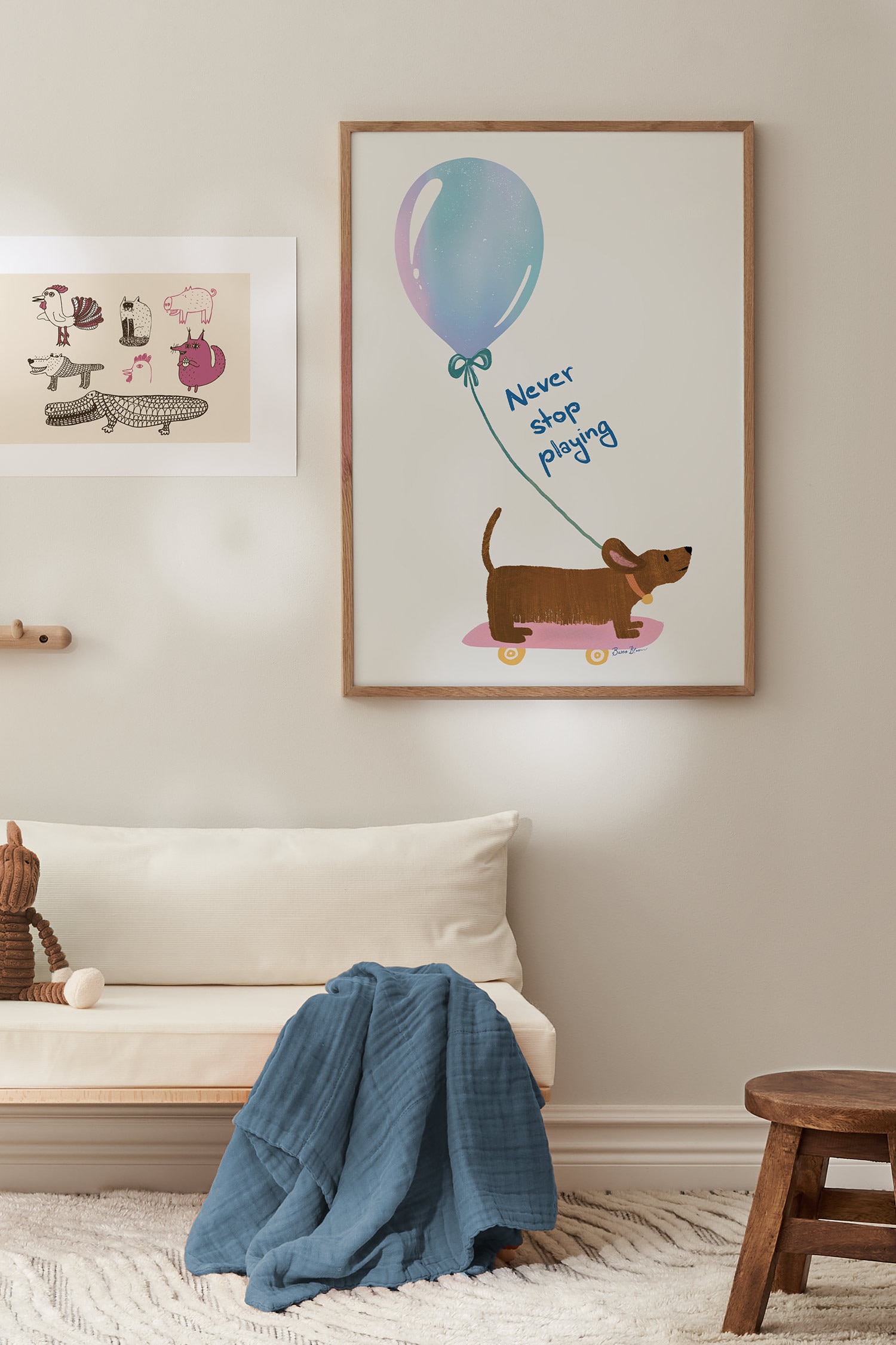 Een kunstprint met een illustratie van een bruine teckel op een roze skateboard met gele wielen tegen een crÃ¨mekleurige achtergrond. Boven de hond zweeft een grote, iriserende blauwe en paarse ballon, verbonden met een groen touwtje, met in het midden de in blauw handgeschreven tekst "Never stop playing".
