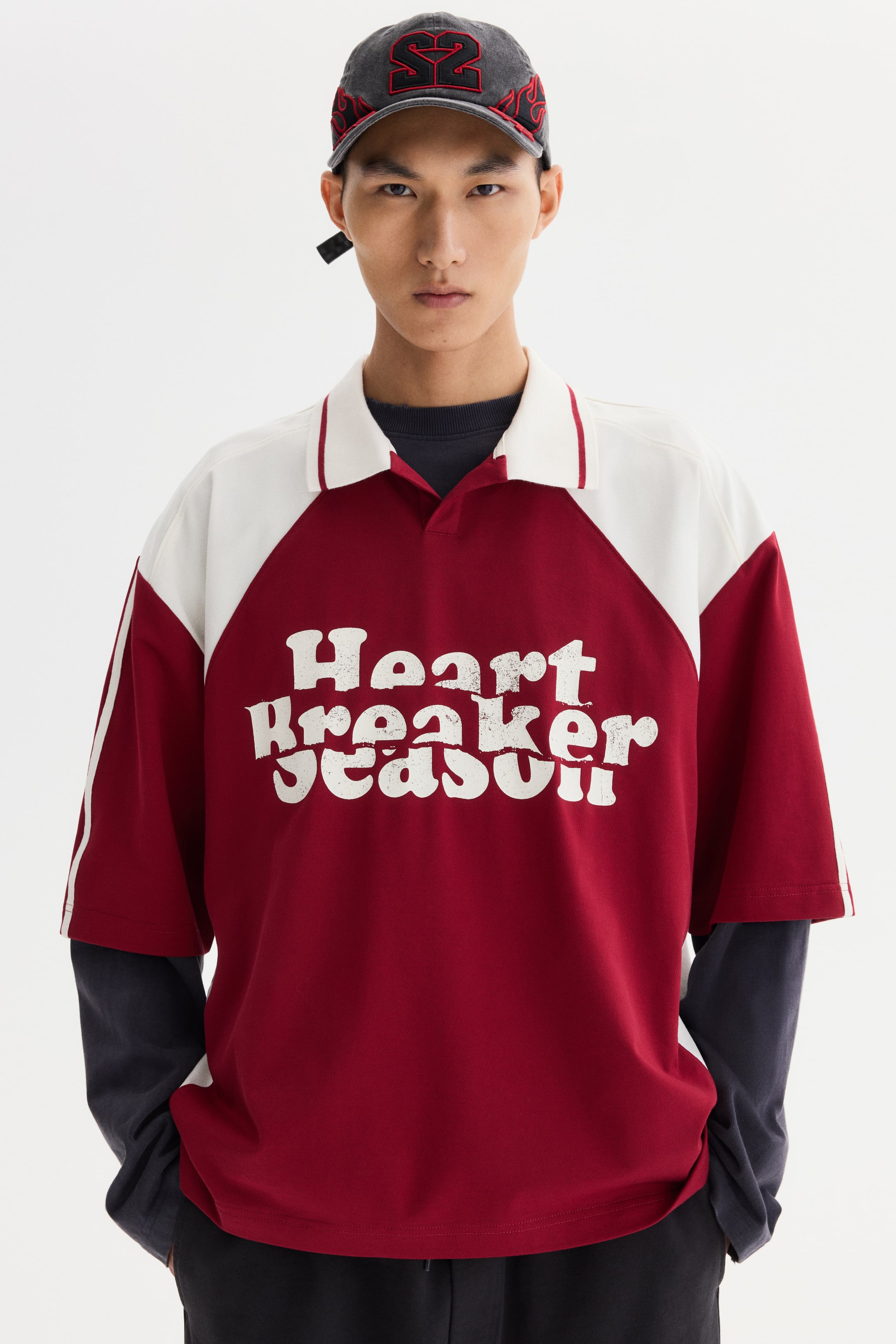 View larger image: A two-tone short-sleeved polo shirt with a maroon body, white raglan sleeves, and a white collar with red stripes is being worn by the model. "Heart Breaker Season" in distressed white lettering is displayed on the front, and the shirt is layered over a dark long-sleeved top.