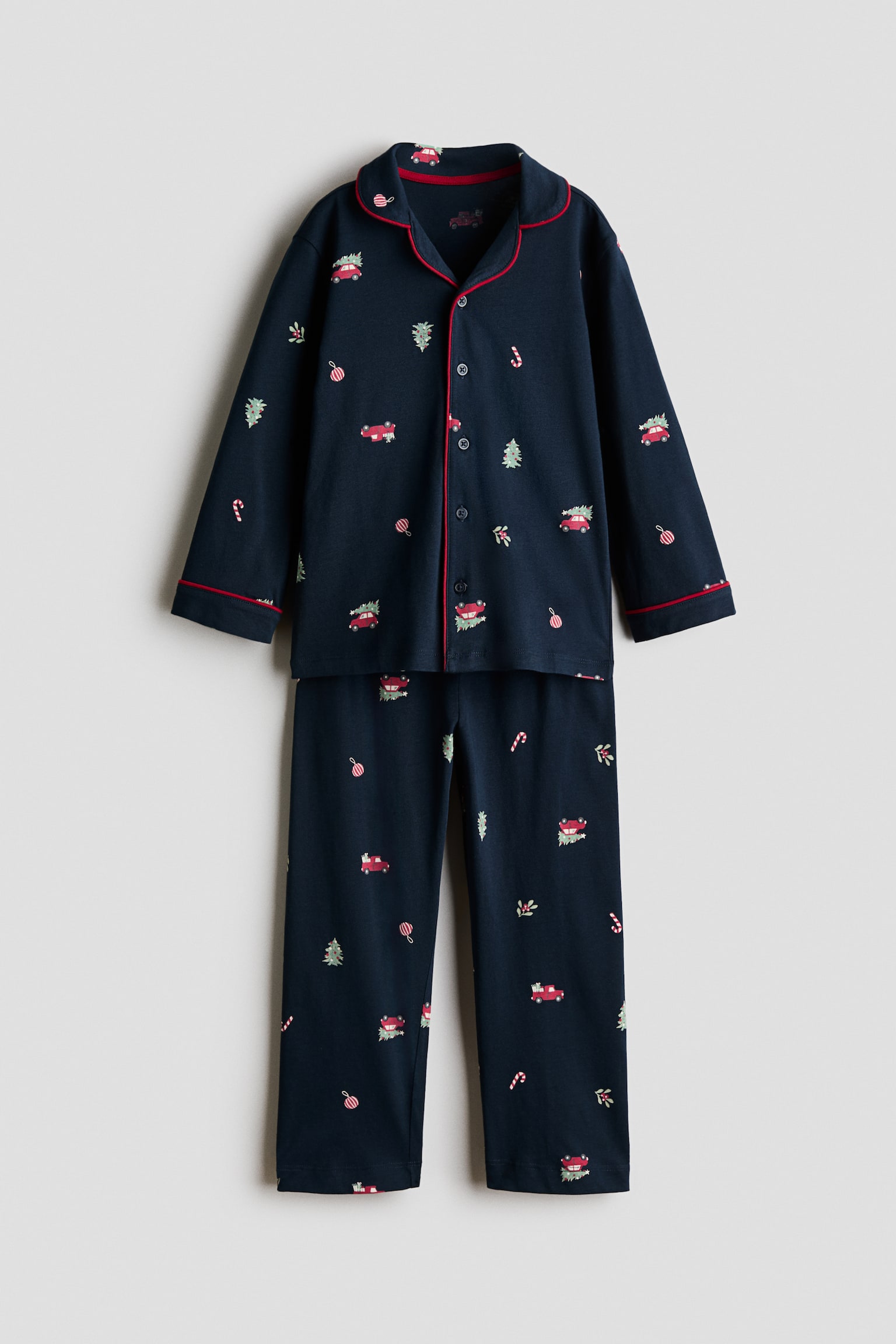 Un ensemble de pyjamas bleu marine est prÃ©sentÃ© de face, composÃ© dâune chemise Ã  manches longues et dâun pantalon assorti, ornÃ©s dâun imprimÃ© festif de voitures et dâarbres. La chemise prÃ©sente un col, une fermeture boutonnÃ©e sur le devant et des poignets soulignÃ©s dâun passepoil rouge, tandis que le pantalon assorti tombe droit en dessous.