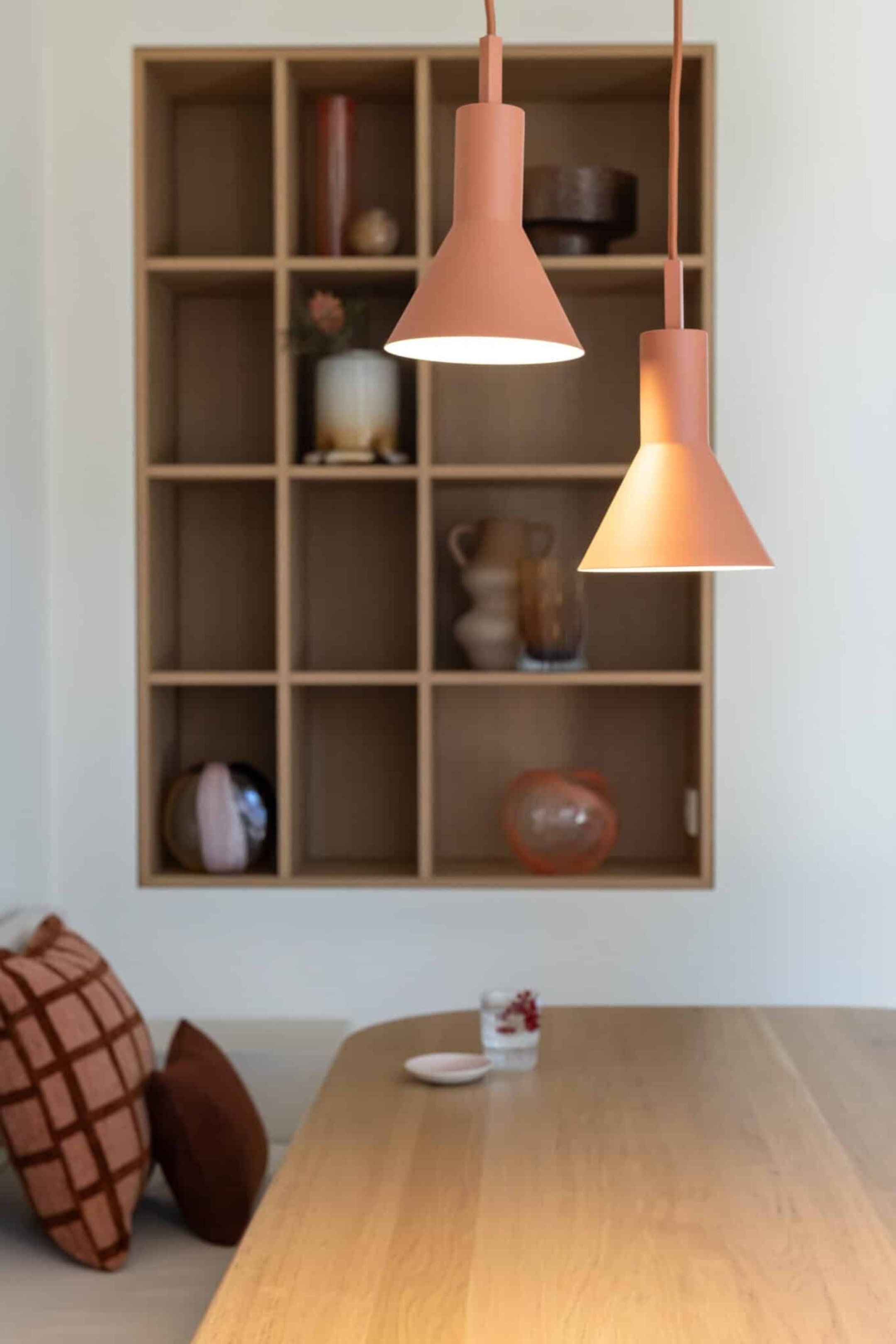 Grotere afbeelding bekijken: Twee Stavanger hanglampen in een matte terracotta-bordeaux afwerking hangen verticaal op verschillende hoogtes en benadrukken hun minimalistische silhouet met een slanke cilindrische bovenkant en een taps toelopende conische kap. De lampen verlichten de ruimte en verspreiden een warme, gouden gloed vanuit hun goudkleurige binnenzijde.