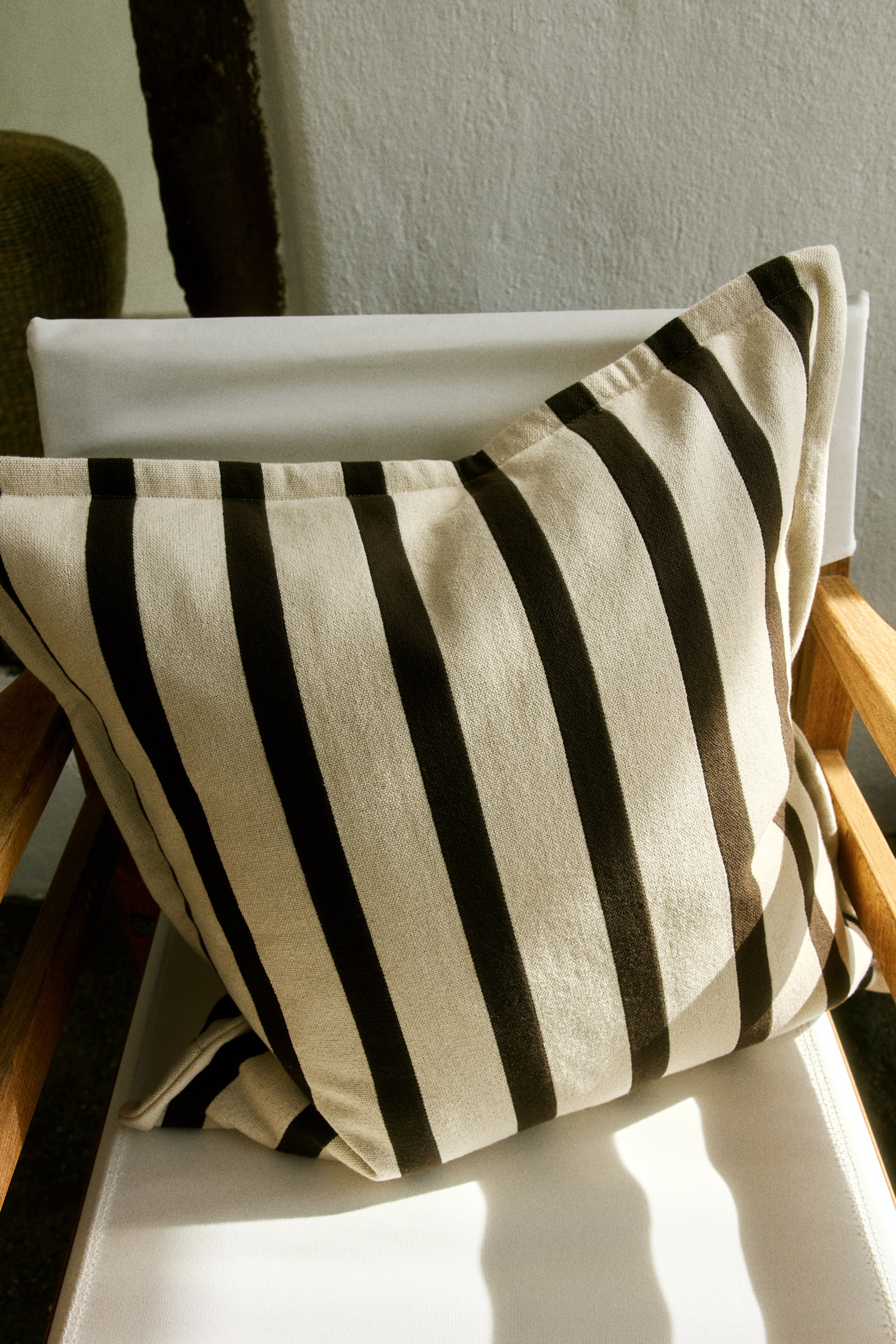 Voir une image plus grande: Une housse de coussin en toile de coton arbore un motif rayé en beige et brun foncé. Sa face avant est inclinée, révélant des rayures verticales.