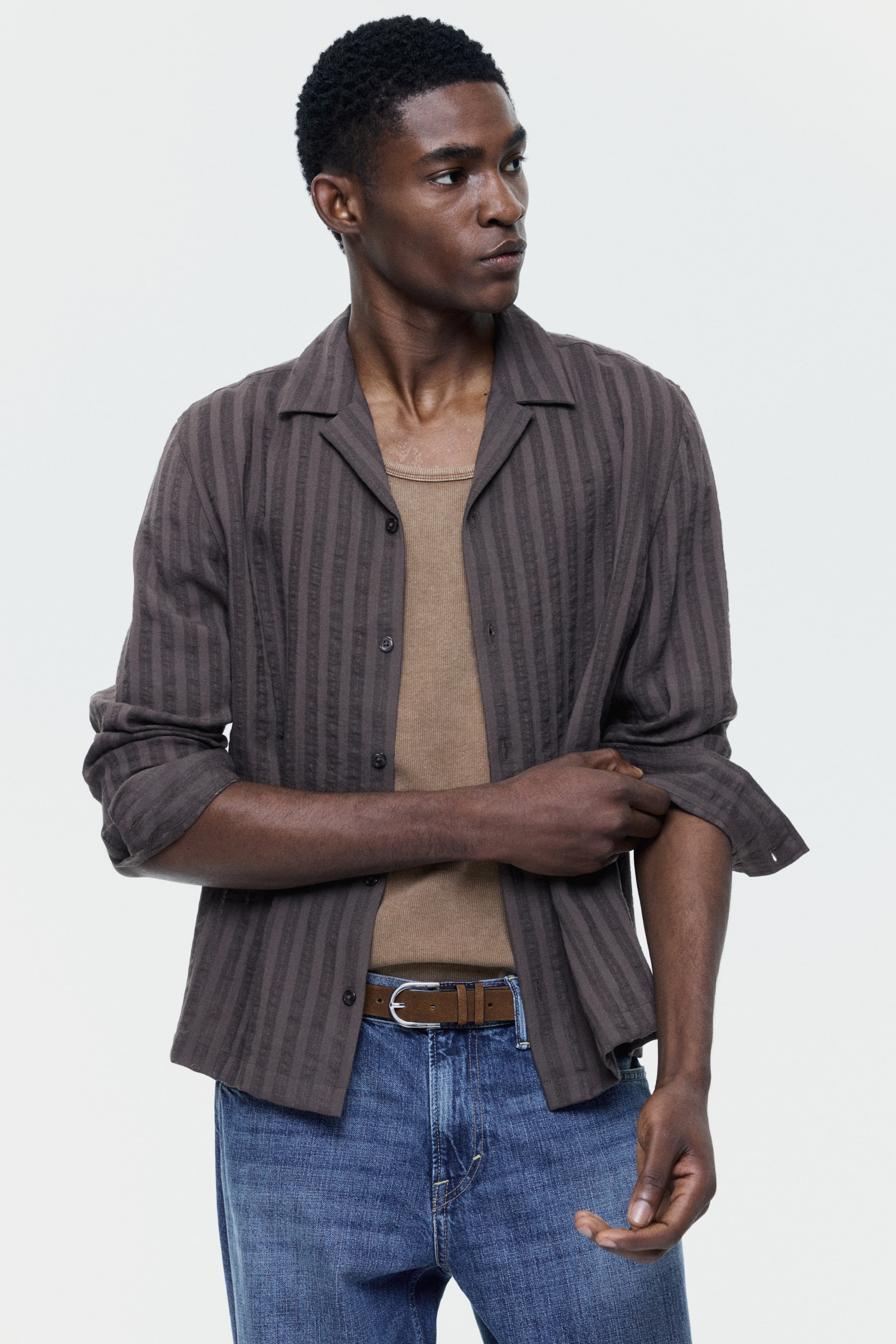 查看大圖: 深棕色条纹衬衫配有古巴领和竖纹纹理条纹。长袖卷起，敞开穿在浅棕色罗纹背心外。