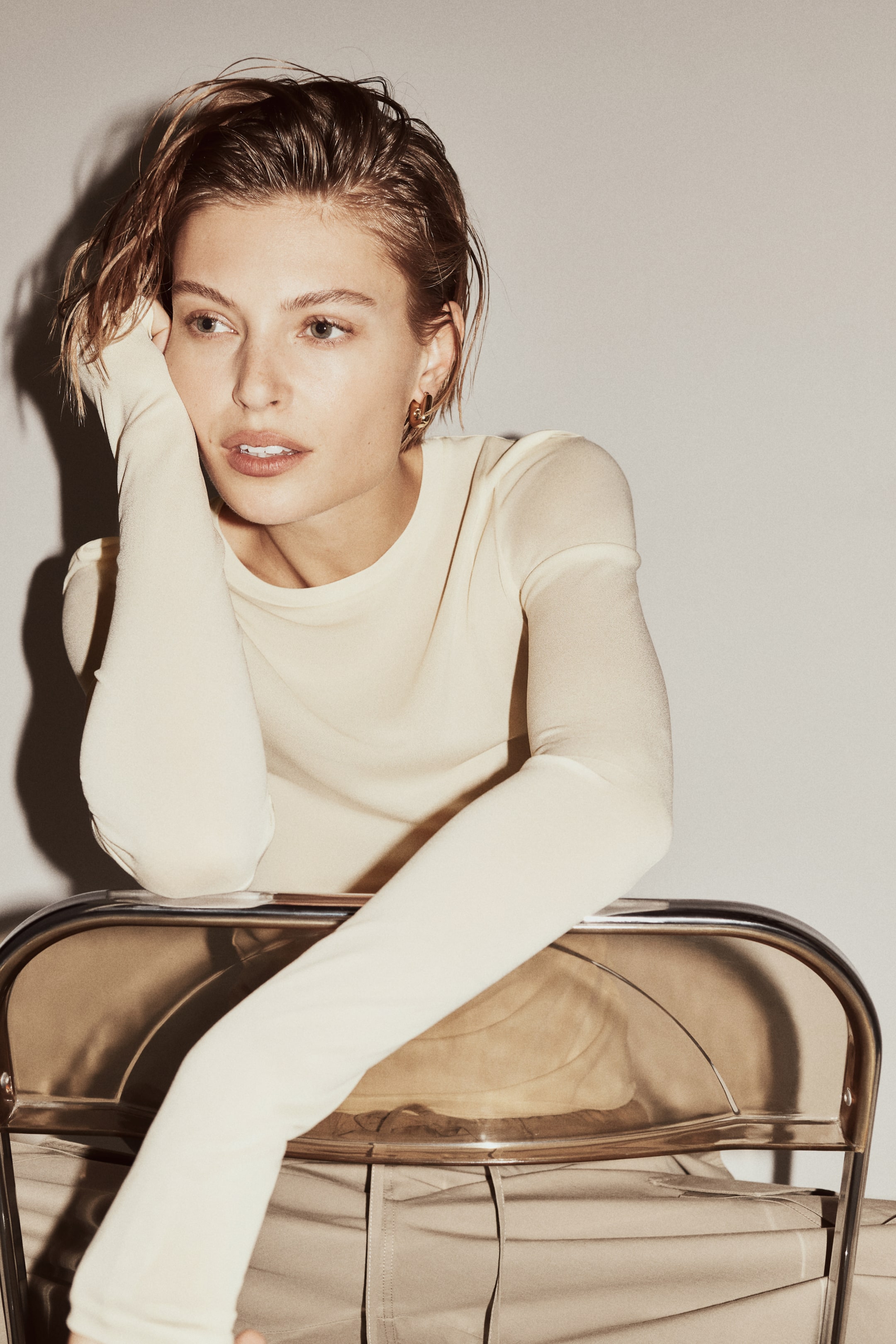 View larger image: A light-cream long-sleeved top fits close to the body, featuring a crew-neck and extra-long sleeves that extend over the hands. Light-tan trousers are visible below, showing a drawstring waist and a relaxed fit.