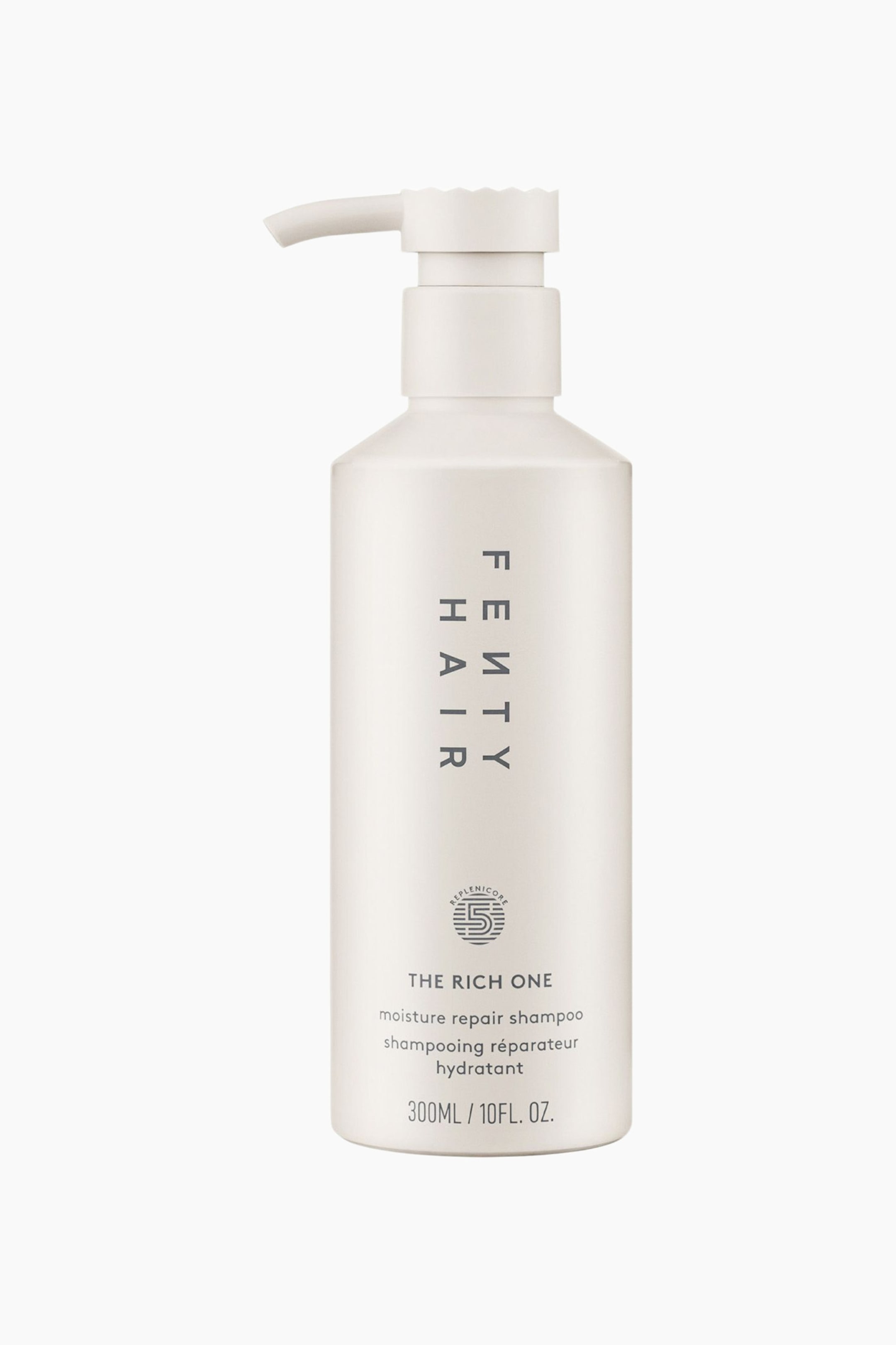 Visa större bild: The Rich One Moisture Repair Shampoo står upprätt i en framåtvänd vy och visar en matt, benvit cylindrisk flaska med en matchande pumpdispenser. På framsidan av flaskan syns vertikal ”FENTY HAIR”-branding, en cirkulär logotyp och produktdetaljer tryckta i mörkgrå text.
