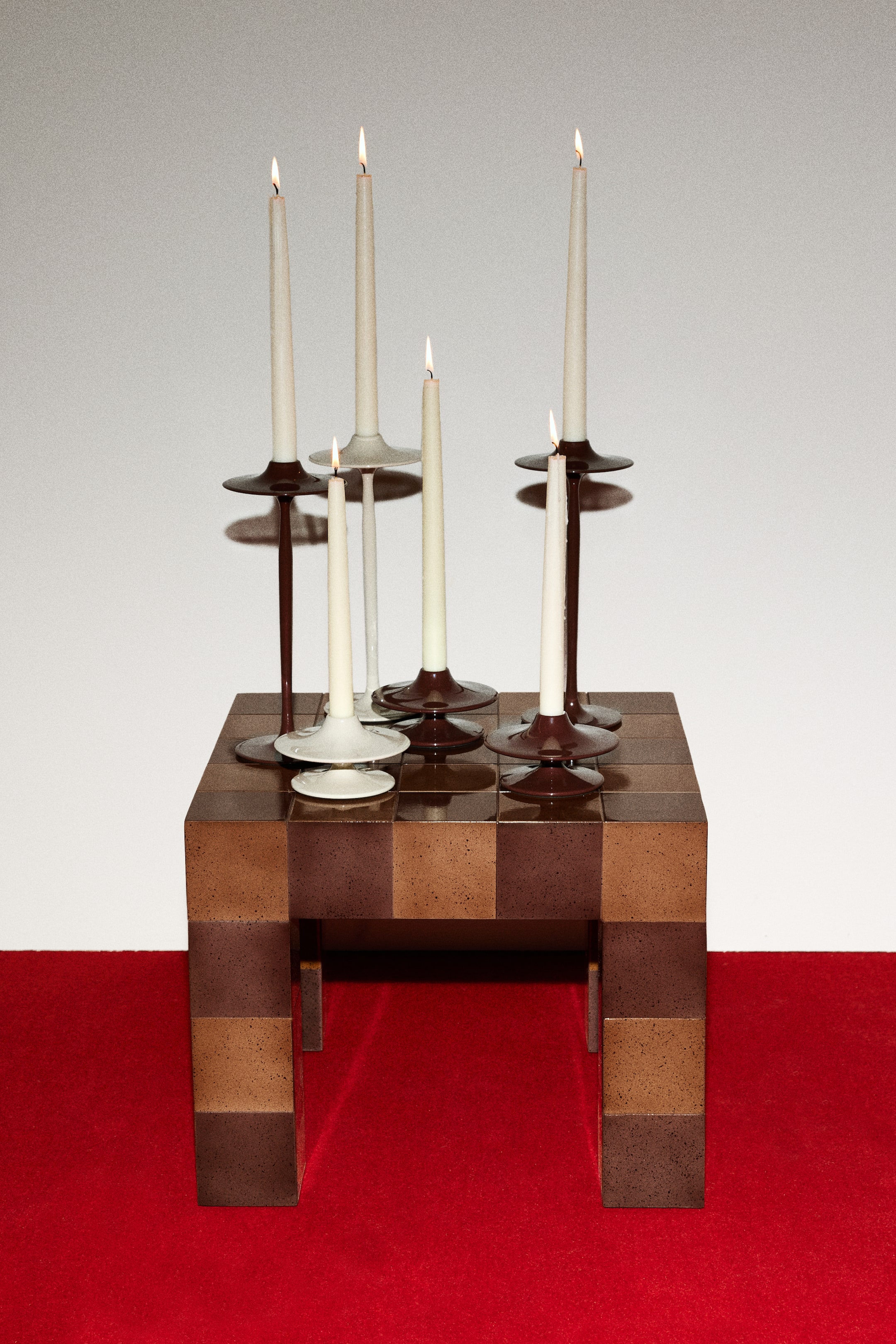 View larger image: Tall candlesticks showcase a sleek design in powder-coated metal with a glossy finish. They come in dark brown and off-white colors, each holding a lit, slender candle.