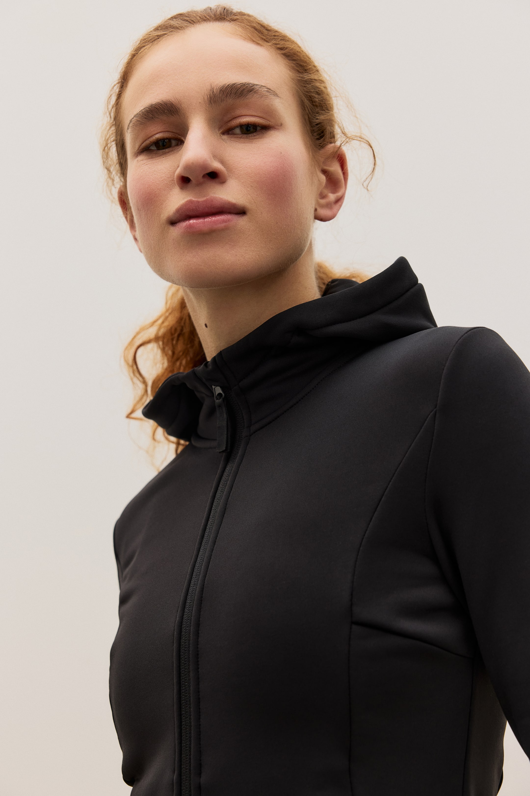 Agrandir l'image: Une veste de sport noire présente une fermeture éclair complète à l'avant et un col montant, avec des coutures ajustées le long du corps et des manches longues visibles sous un angle avant-droit.