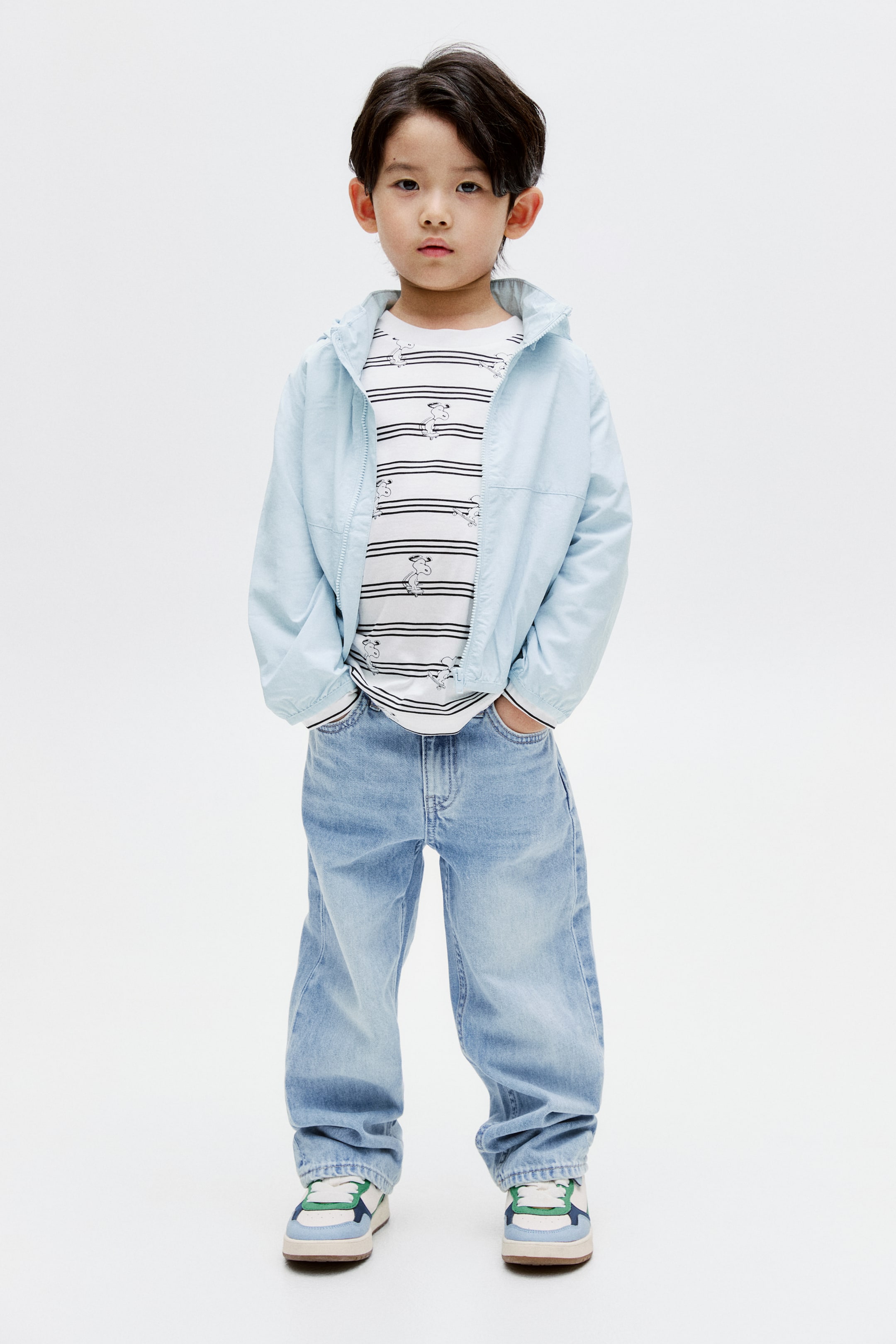 View larger image: An outfit, presented facing forward, showcases a light blue hooded jacket, partially zipped over a white t-shirt with black horizontal stripes and small Snoopy characters. Light wash relaxed fit jeans complete the look, paired with white sneakers detailed with blue, green, and navy accents.