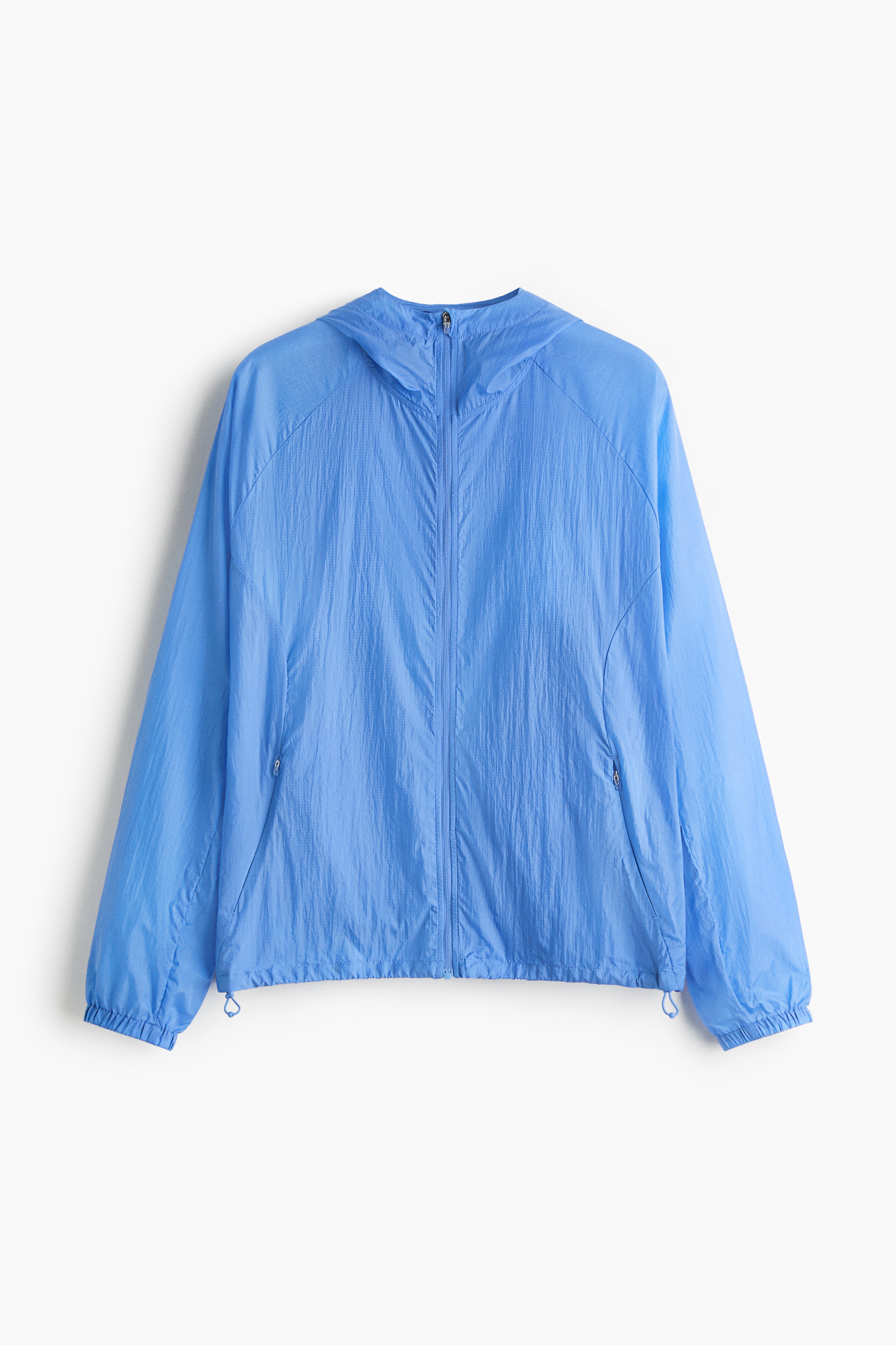 Eine blaue Laufjacke mit entspannter Passform wird vom Model getragen und Ã¼ber einem weiÃen Langarmshirt sowie einer schwarzen Leggings kombiniert. Die leichte Jacke verfÃ¼gt Ã¼ber eine Kapuze, elastische ÃrmelbÃ¼ndchen und einen sichtbaren Kordelzug am Saum.