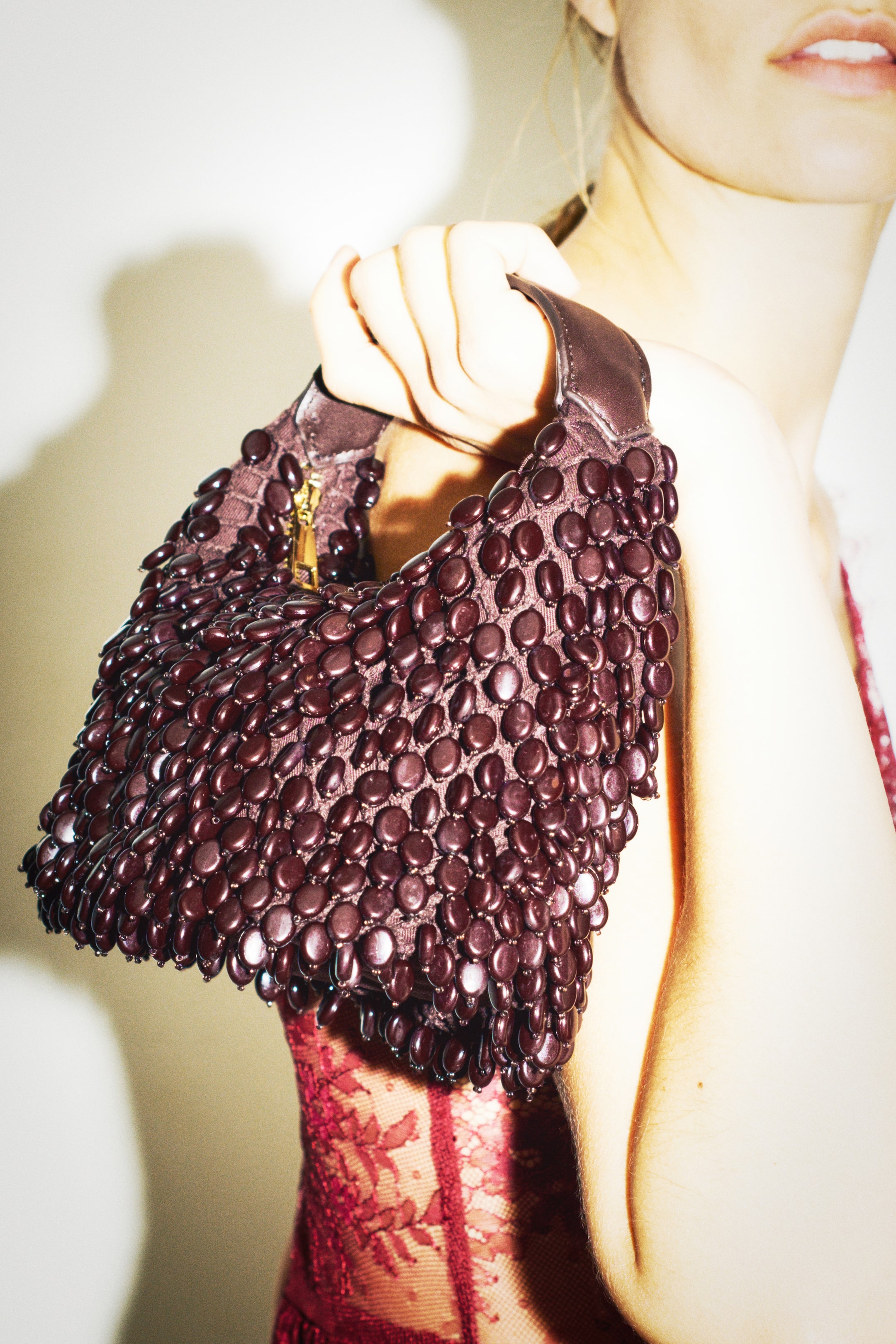 View larger image: A model is holding a dark brown handbag covered in glossy, oval-shaped plastic beads, showing the front design. The handbag features a wide, smooth coated fabric handle and a gold-toned zipper at the top.