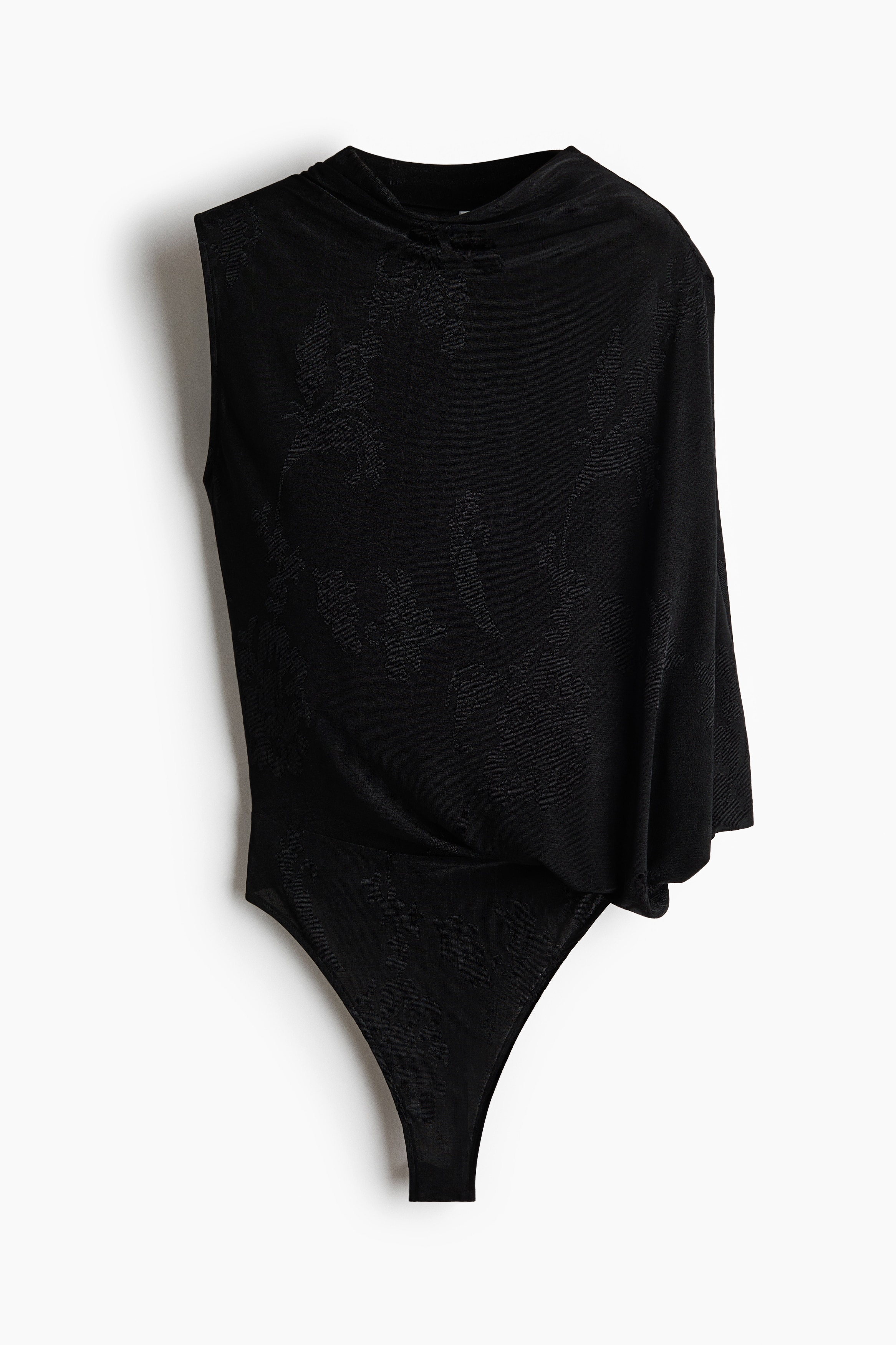 Ein dunkel gestrickter Jacquard-Jersey-Body wird vom Model getragen und verfÃ¼gt Ã¼ber einen runden Ausschnitt, einen kurzen Ãrmel auf einer Seite sowie einen drapierten Cape-Ãrmel auf der anderen. Das Model posiert mit erhobenen Armen und kombiniert den Body mit tief sitzenden, aufgeknÃ¶pften Jeans, die den hoch geschnittenen HÃ¼ftbereich betonen.