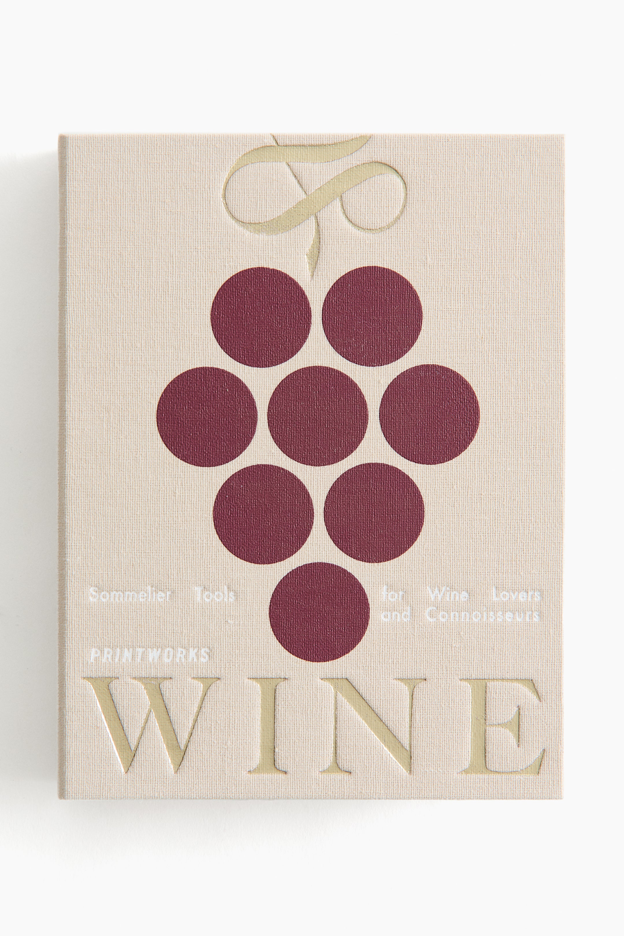 Ver imagem maior: Um livro de capa dura apresenta uma capa de tecido bege. A frente apresenta um floreado dourado em relevo no topo, um conjunto de sete círculos vermelho-escuro formando um cacho de uvas, e texto branco que diz "Sommelier Tools," "for Wine Lovers and Connoisseurs," e "PRINTWORKS." A palavra "WINE" está gravada em relevo em grandes letras douradas na parte inferior.