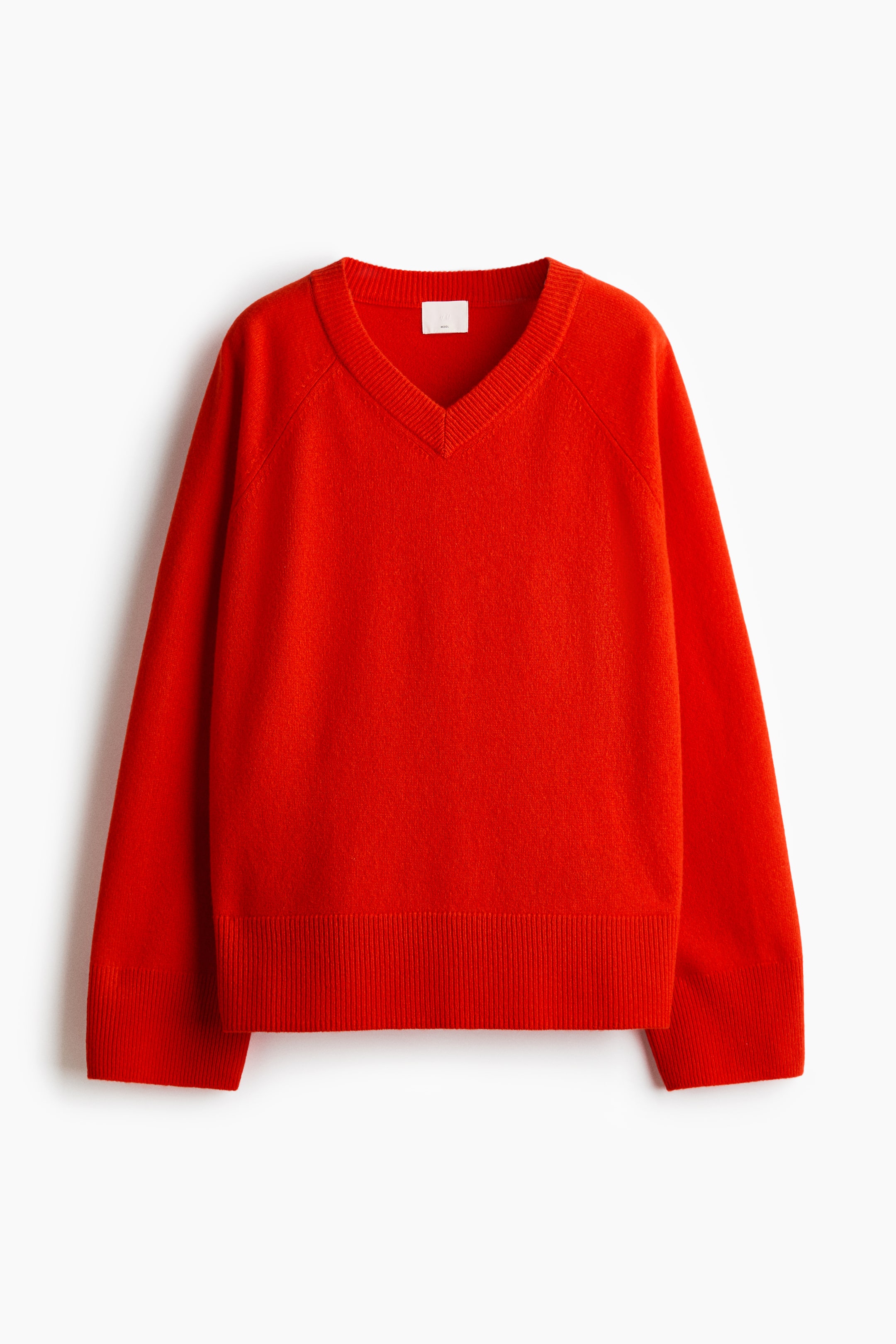 View larger image: The red, oversized sweater is shown from the front, highlighting its soft knitted wool construction, ribbed V-neckline, long raglan sleeves, and ribbed cuffs and hem.