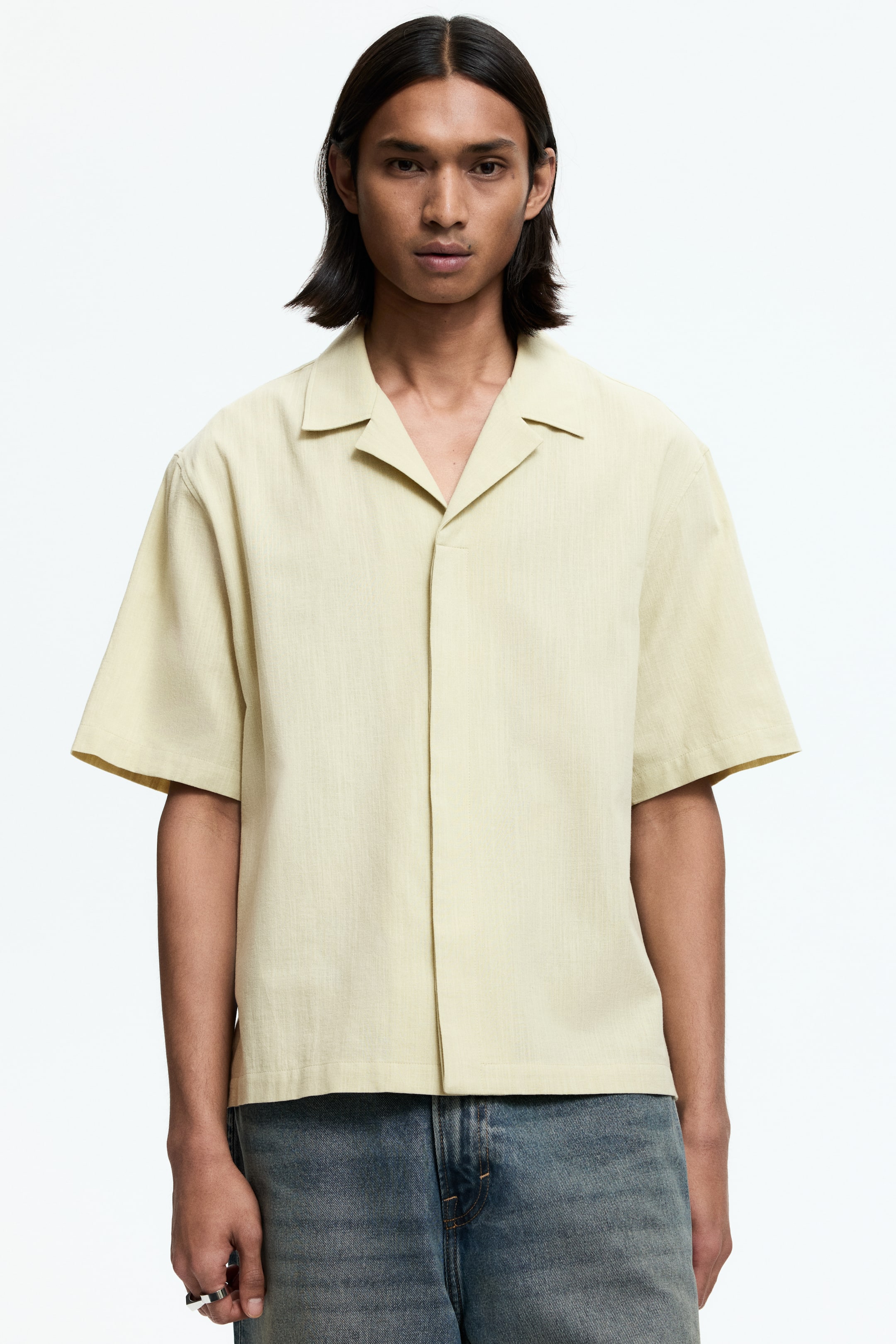 View larger image: A light yellow short-sleeved shirt featuring a revere collar, a subtle vertical texture, wide loose sleeves, and a clean, buttonless front placket, presenting a relaxed, untucked fit.