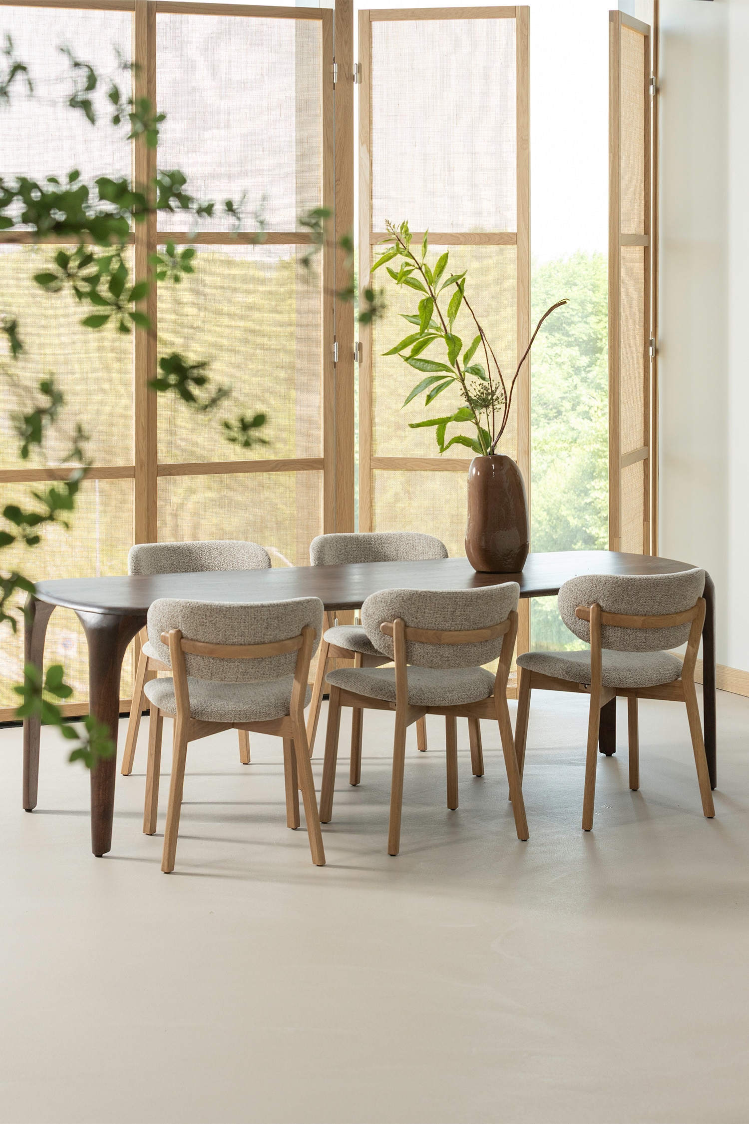 Une table en bois foncé est présentée d'une perspective légèrement élevée et de face. Elle présente un plateau rectangulaire avec des coins légèrement arrondis et quatre pieds, dont les deux extérieurs descendent en douceur depuis les extrémités du plateau.