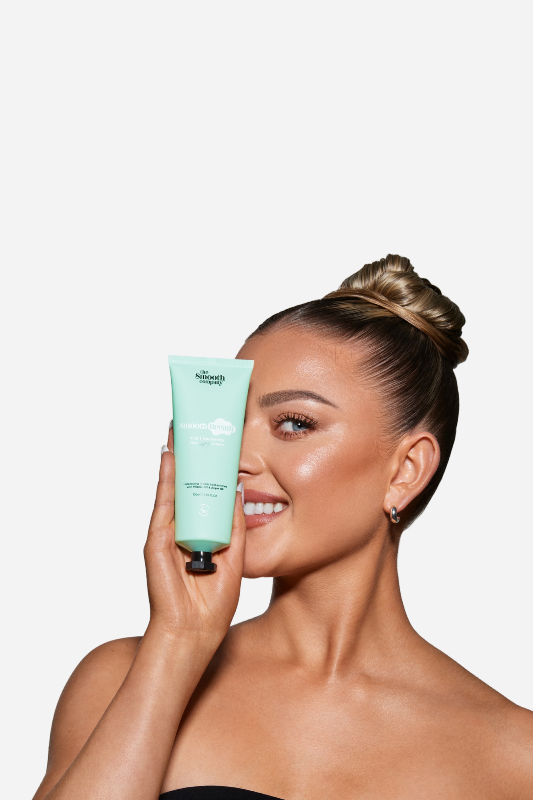 Vis større bilde: En mintgrønn tube av "the smooth company smooth Cream" holdes vertikalt av en hånd. Forsiden av etiketten, som viser merkevarenavnet, produktnavnet og teksten "100ml / 3.38 FL OZ", vender fremover, og den har en svart kork nederst.
