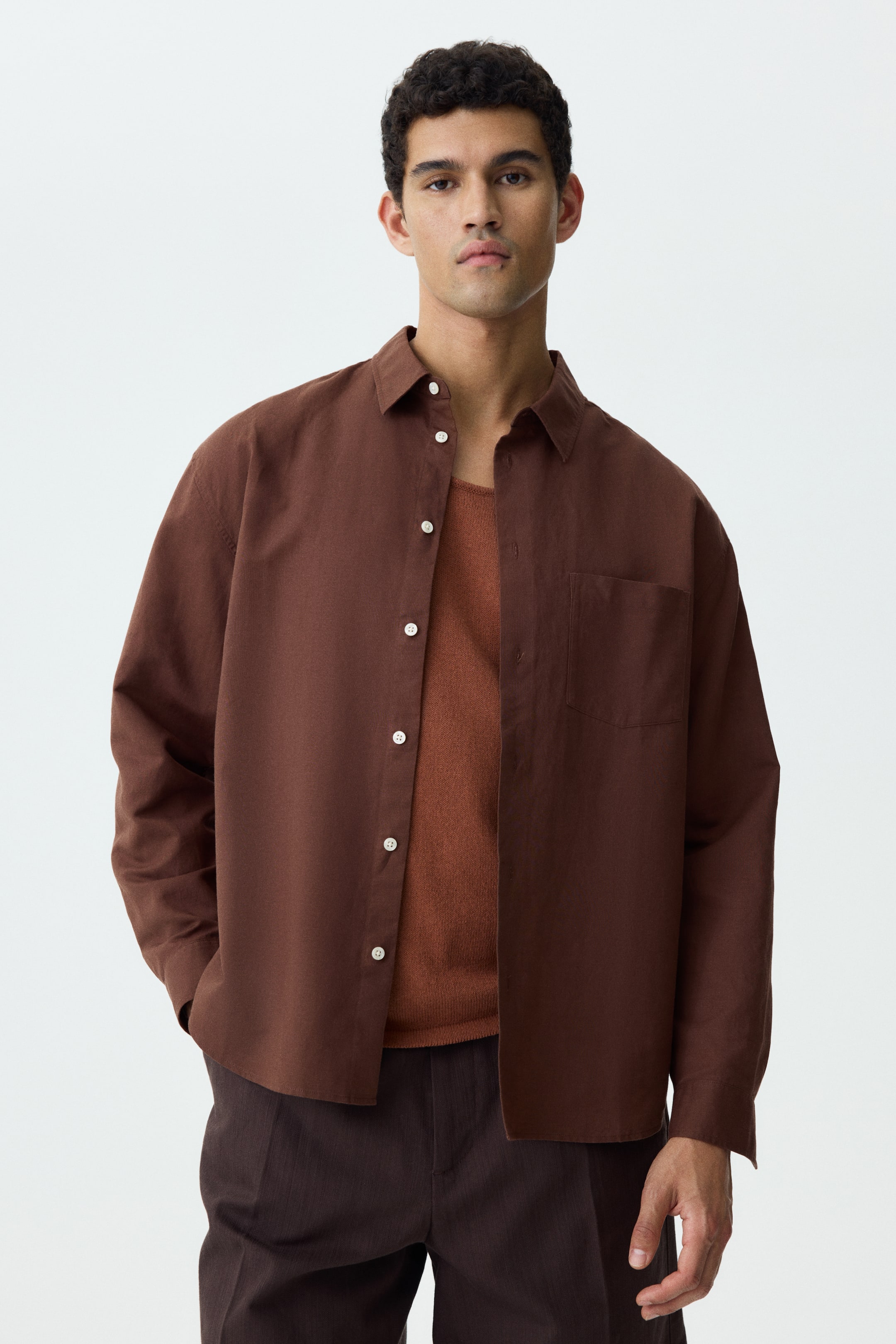 View larger image: The brown shirt comes with a spread collar, white buttons, and a single patch pocket on the left chest. It offers a relaxed fit with long sleeves and is styled open over a rust-coloured top.