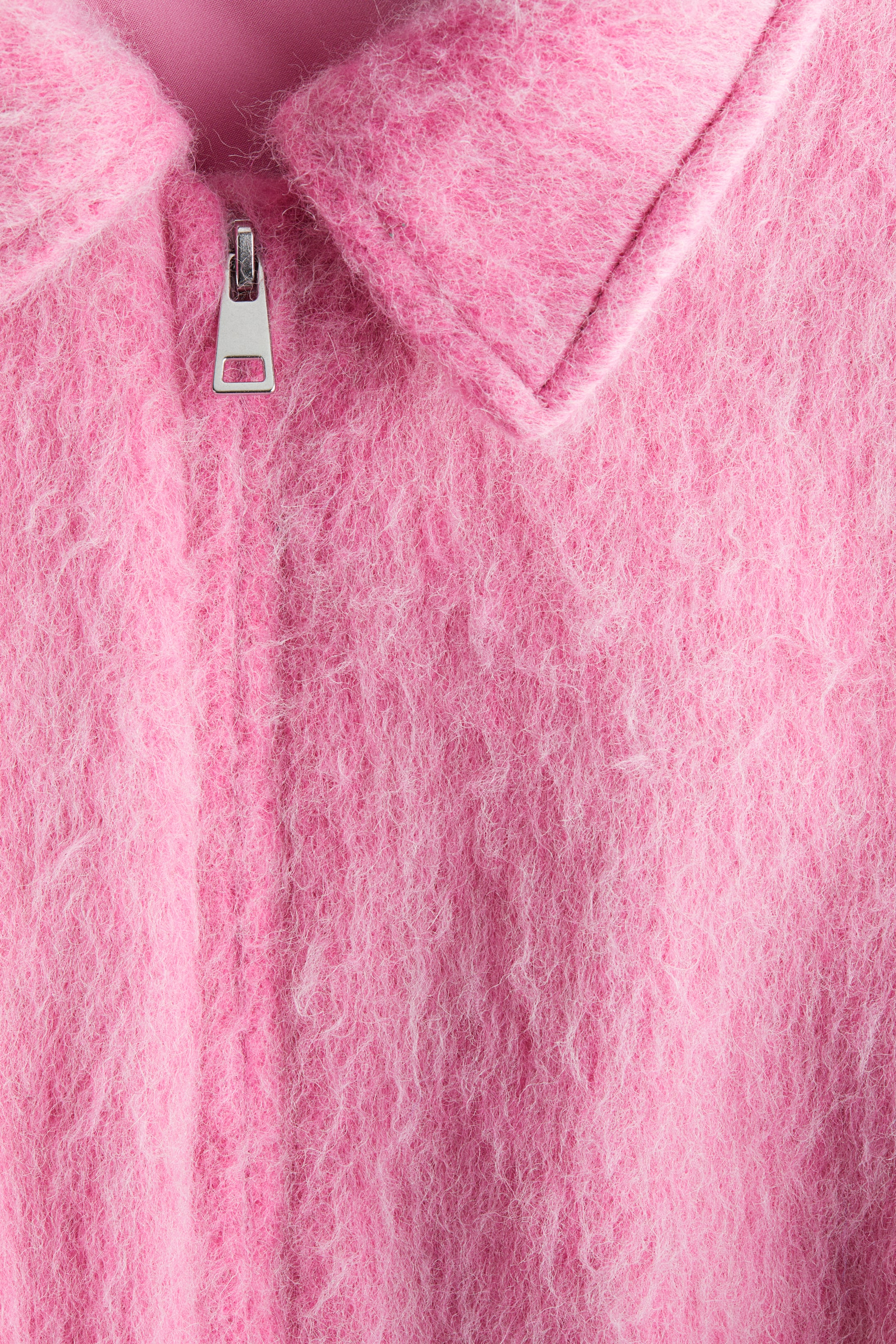 Agrandir l'image: Un vêtement rose duveteux présente un curseur de fermeture éclair de ton argenté au centre avant, positionné sous un col pointu. Le tissu présente une texture longue et pelucheuse.