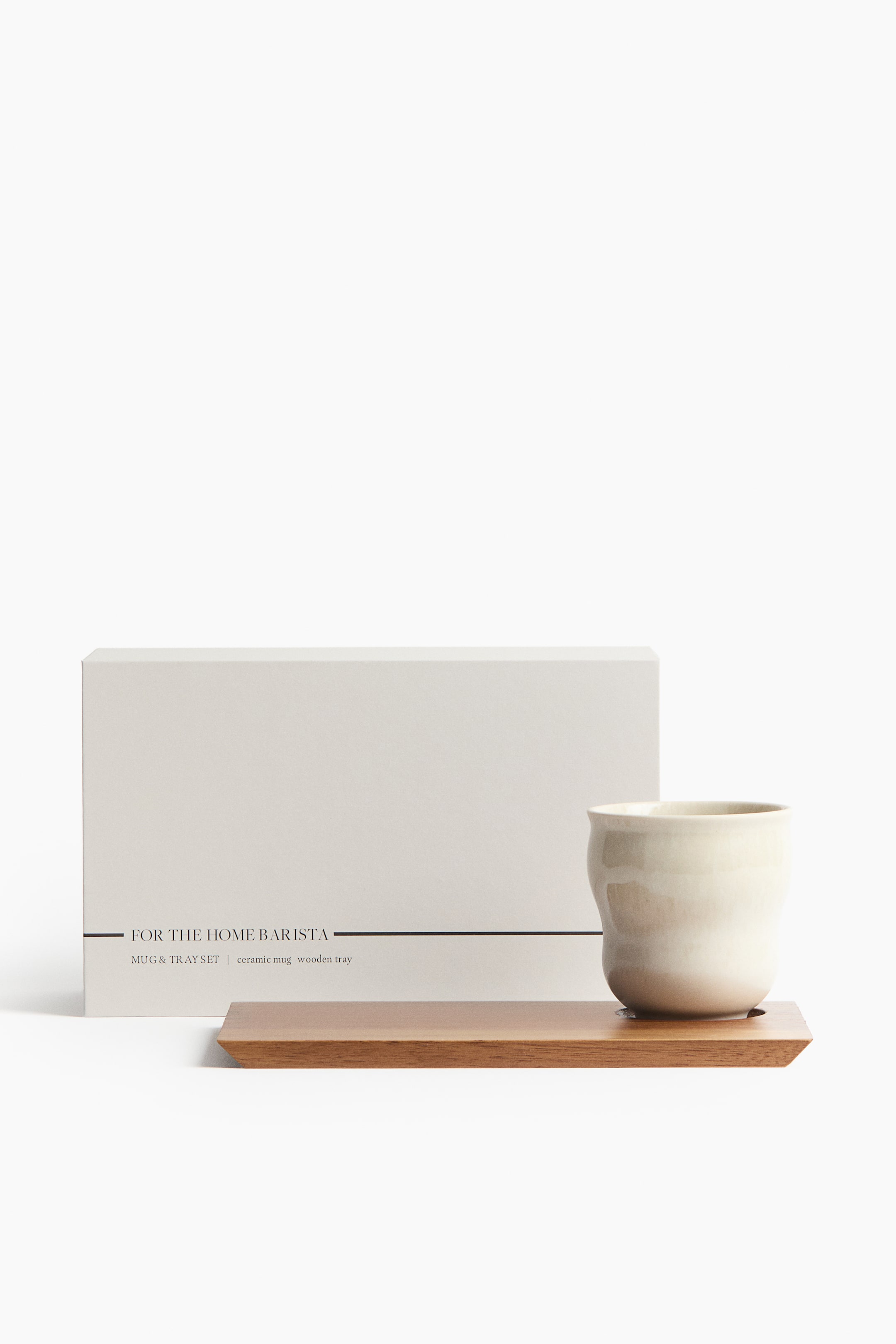 View larger image: This gift set showcases an off-white stoneware mug with a reactive glaze, characterized by its irregular shape and subtle colour variations, elegantly placed on a rectangular acacia wood tray. A light-coloured gift box stands behind the set, featuring text on the front that reads 'FOR THE HOME BARISTA' and 'MUG & TRAY SET'.