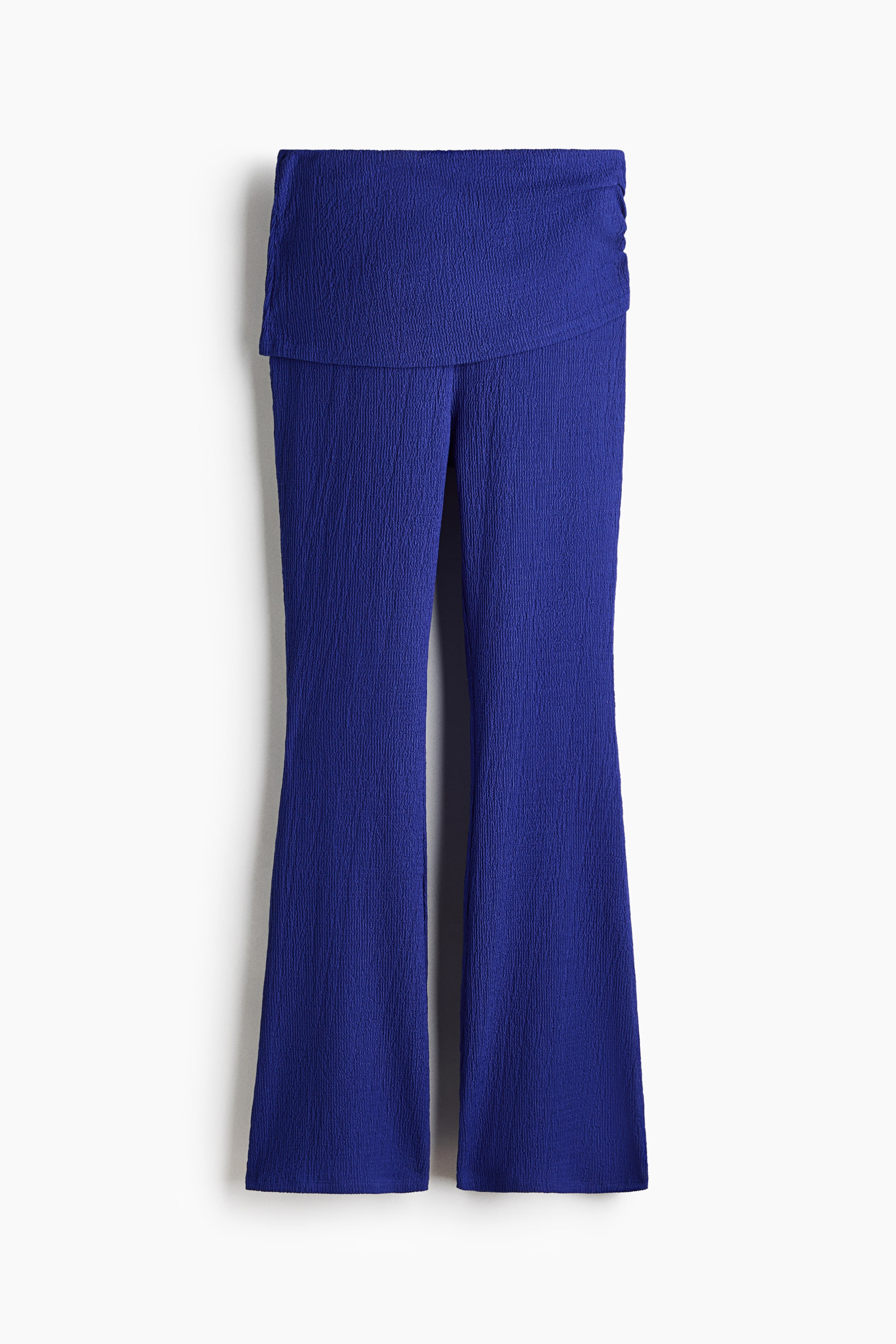 View larger image: Blue trousers showcase a crinkled texture all over, crafted with a high, wide waistband that overlaps at the front and is gently gathered on the right side. The legs fit snugly through the thigh and flare out to a wide hem.