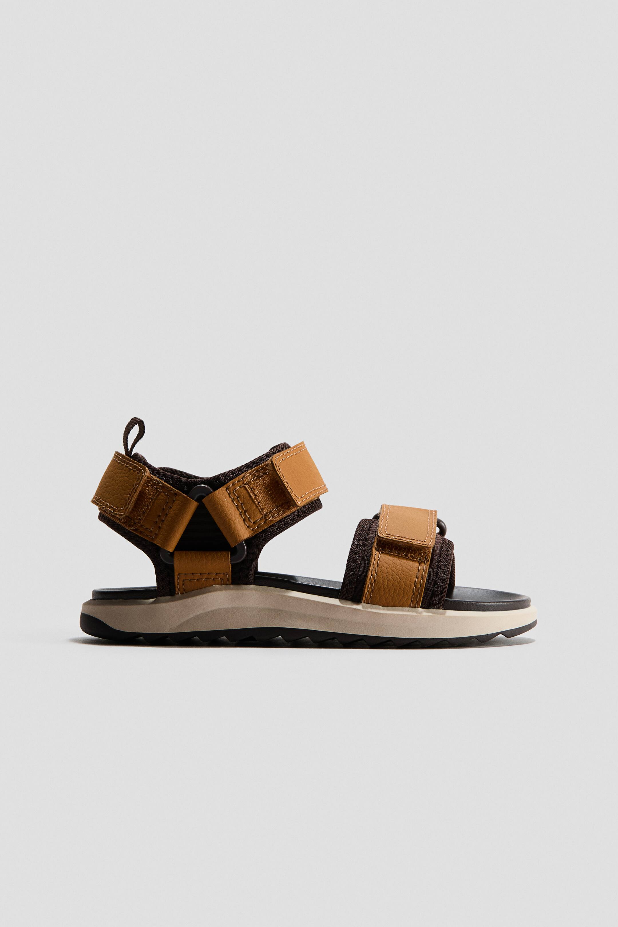 View larger image: This utility sandal showcases multiple brown textured straps alongside dark brown textile straps, all adjustable with convenient hook-and-loop fasteners. It features a layered sole comprising a black footbed, a beige midsole, and a black treaded outsole, displayed in a side profile.