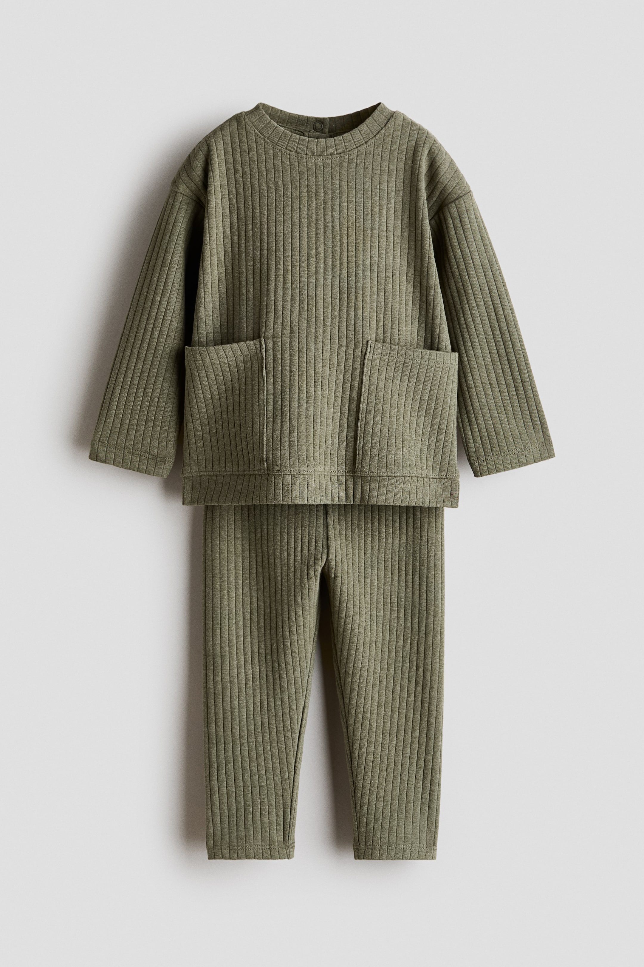 View larger image: A front-facing olive green ribbed jumper and matching leggings set is being showcased. The jumper features a round neckline, long sleeves, and two oversized patch pockets at the front, while the full-length leggings complete the set.
