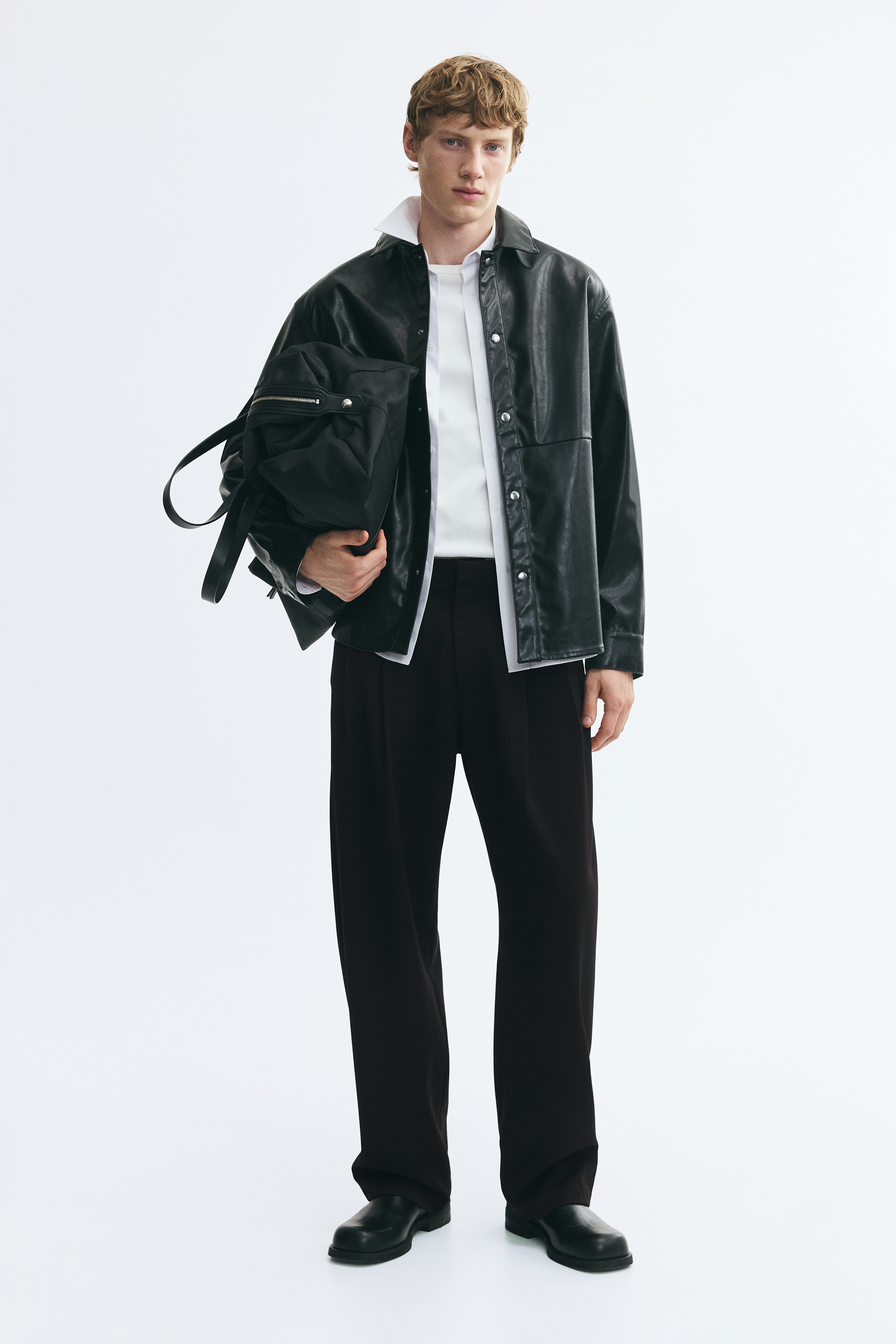 A pair of black trousers is shown from the front, featuring a structured waistband with belt loops and double pleats extending down wide, straight legs.