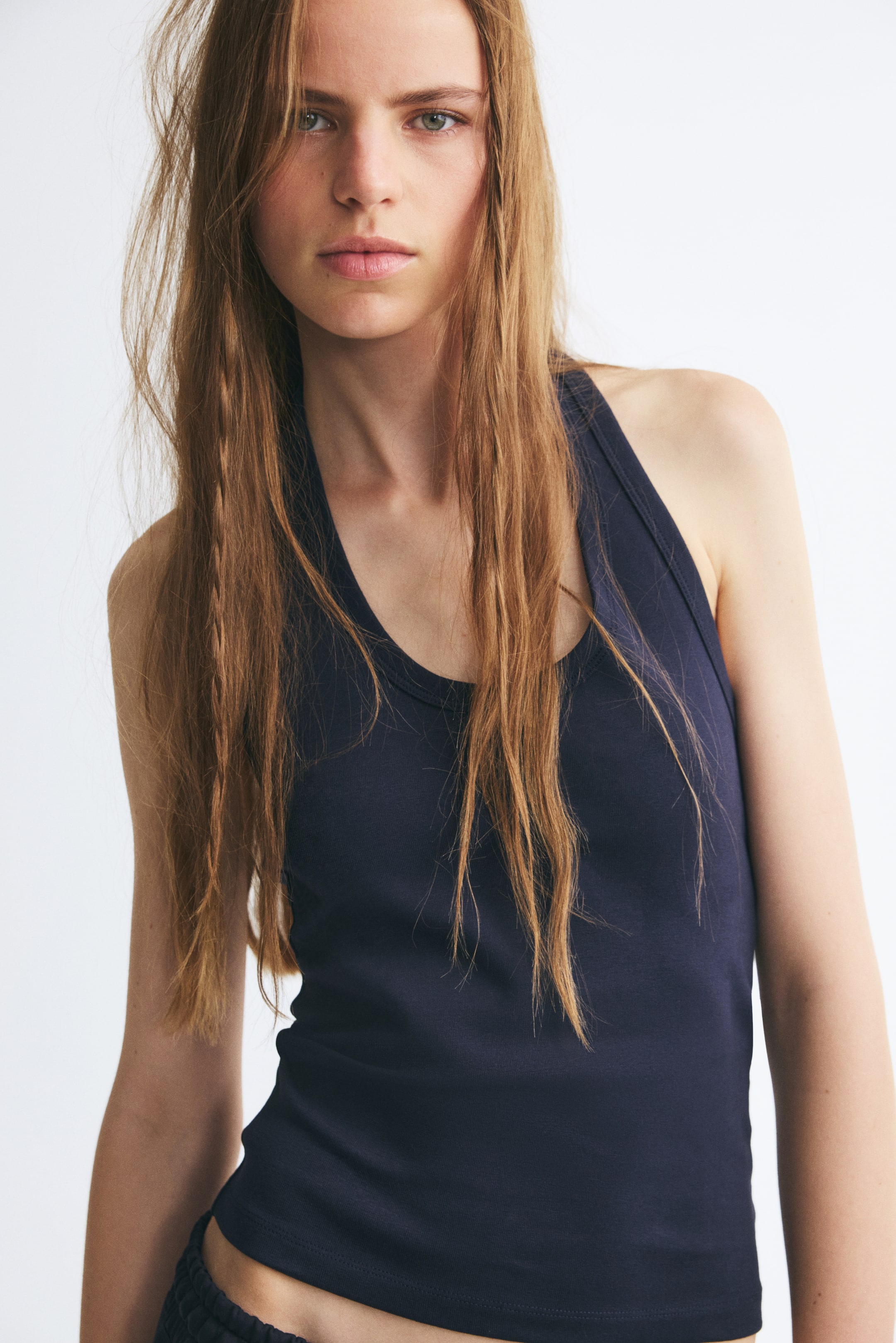 View larger image: A dark blue fitted halter neck top featuring a crew neckline is being worn by the model. The top has a narrow ribbed texture and is styled with a pair of dark pants, showing only the waistband at the bottom.