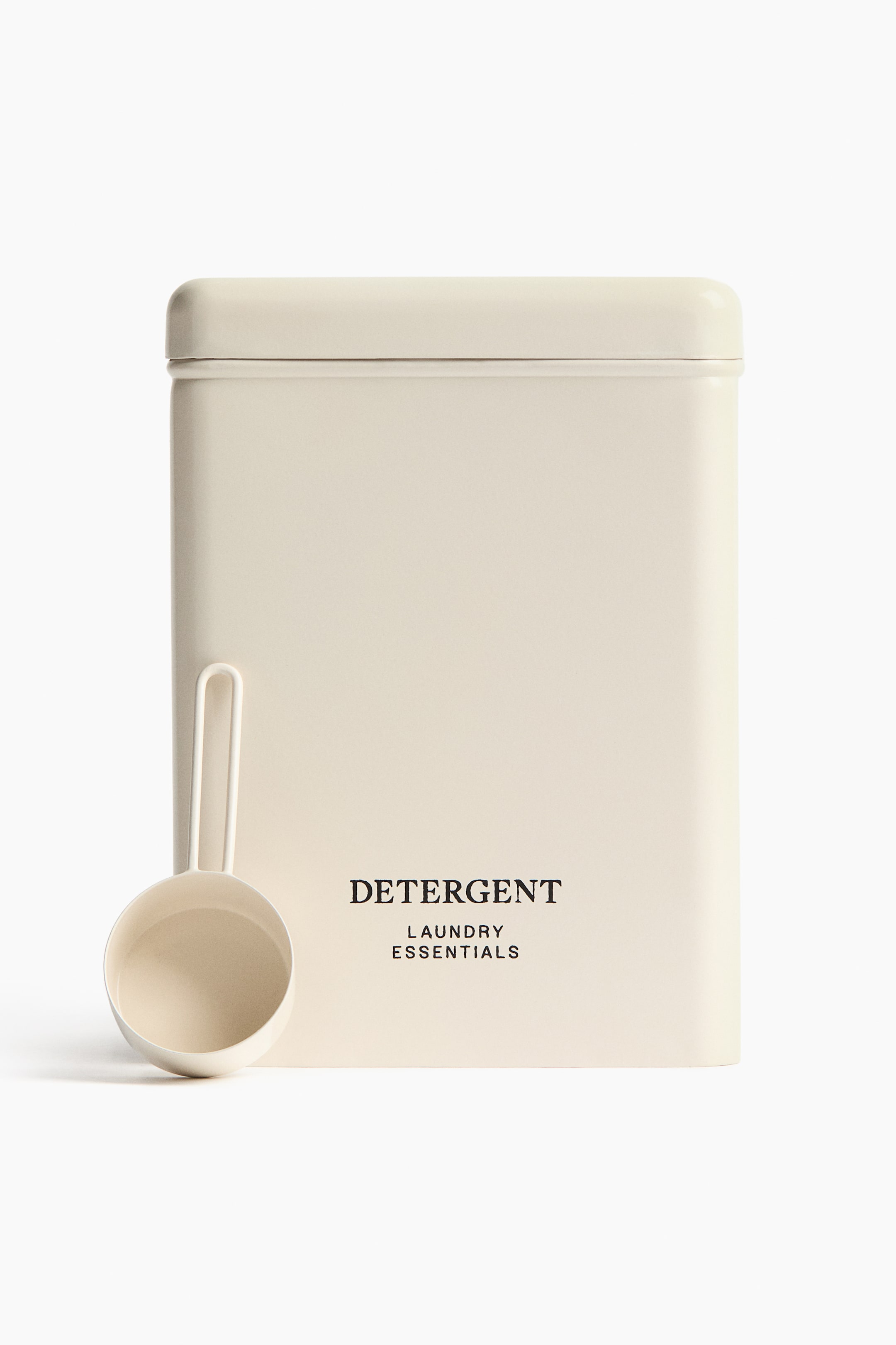 View larger image: An off-white rectangular detergent container stands at the forefront, its top sealed with a fitted lid featuring rounded edges. Black text adorns its front, stating "DETERGENT" above "LAUNDRY ESSENTIALS," while an off-white measuring scoop with a handle rests against its lower left front.