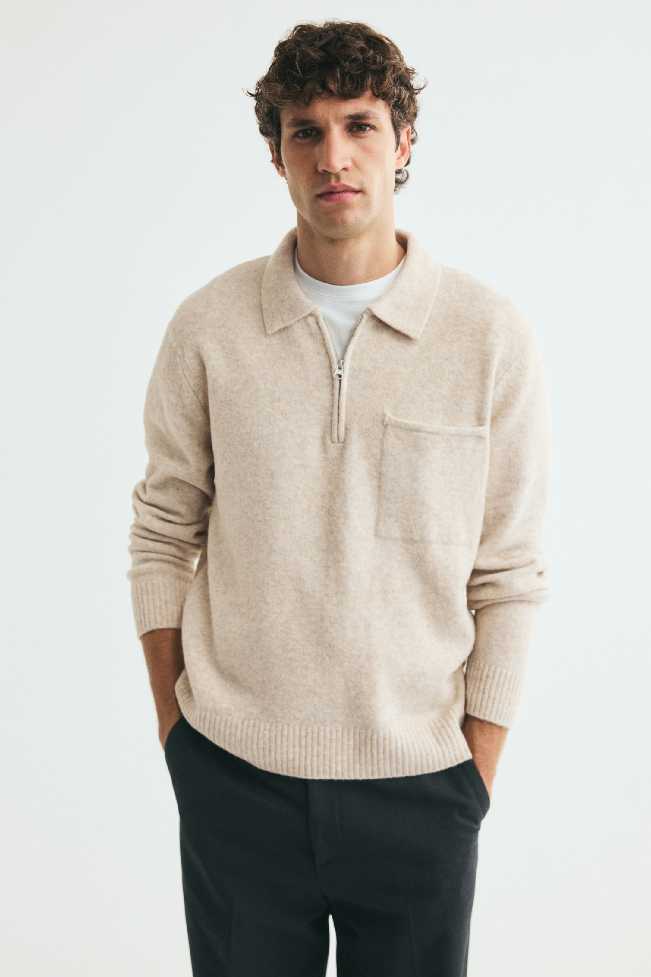 View larger image: A beige knit polo shirt with a collar, half-zip closure, and open chest pocket is worn by the model over a white crew-neck T-shirt. The regular-fit, long-sleeved shirt features ribbed cuffs and a ribbed hem, styled with dark trousers.