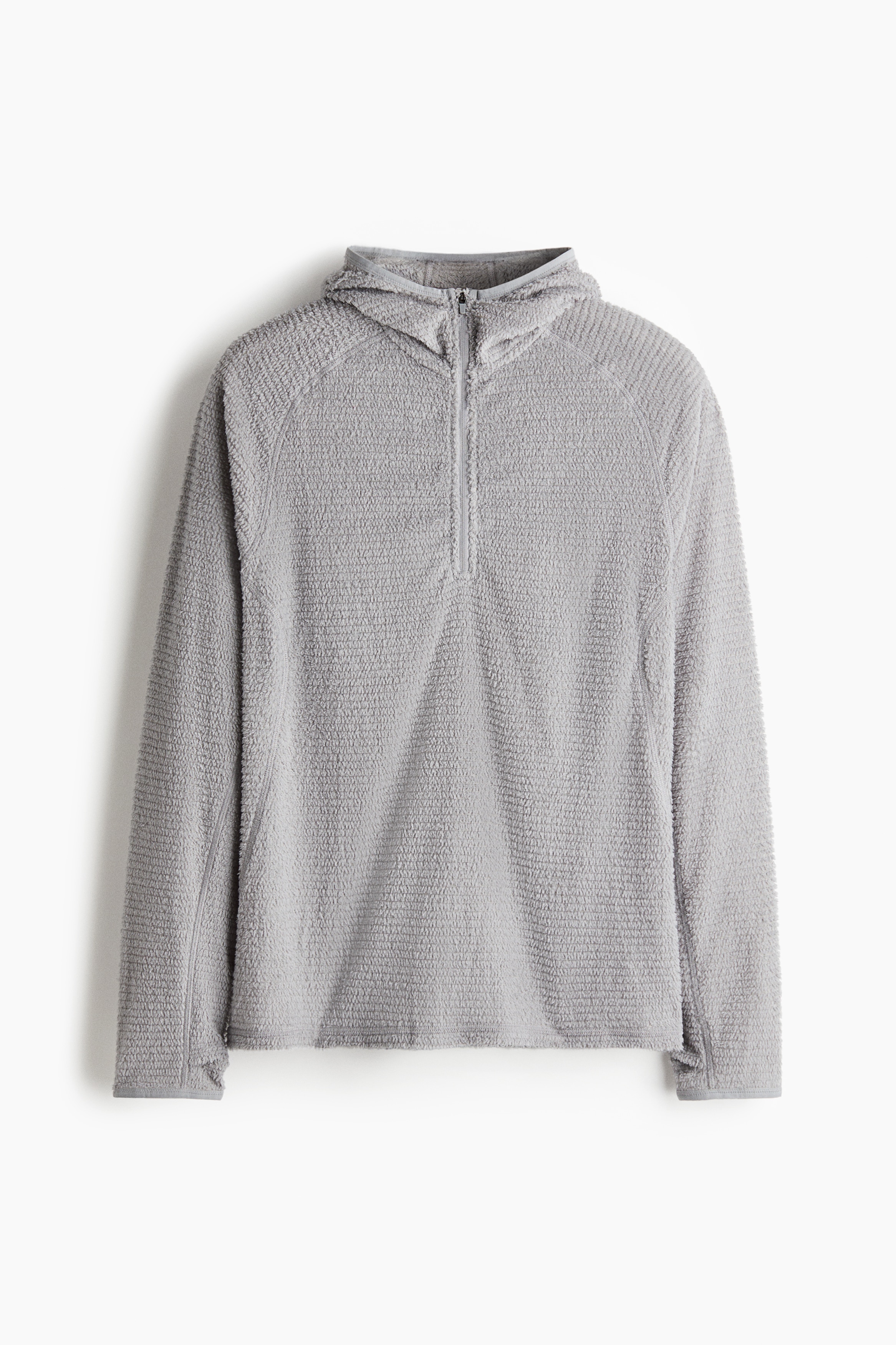Một chiếc áo hoodie vải nỉ có kết cấu, màu xám nhạt, với thiết kế khóa kéo nửa thân đang được người mẫu mặc, mũ trùm đầu kéo lên. Khóa kéo được mở một phần, để lộ phần cổ áo thun trắng bên trong.