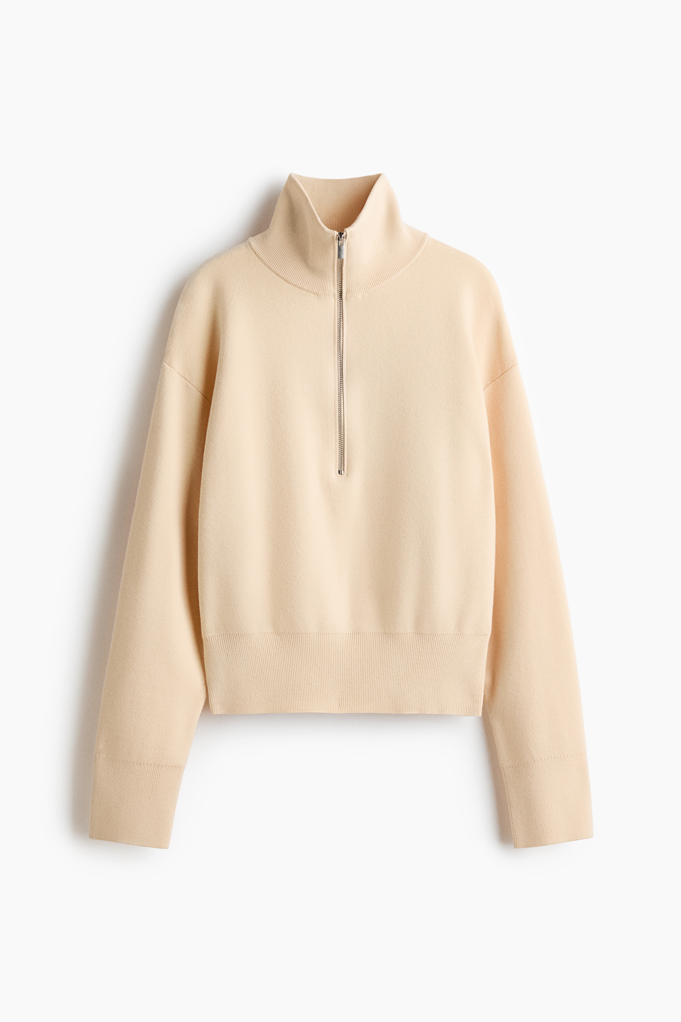Un pull en maille fine couleur crÃ¨me est prÃ©sentÃ© de face, avec un col montant muni d'un demi-zip partiellement ouvert et des Ã©paules tombantes. Le pull prÃ©sente des manches longues avec des poignets cÃ´telÃ©s et un ourlet cÃ´telÃ© arrivant au-dessus de la ceinture d'un jean noir.