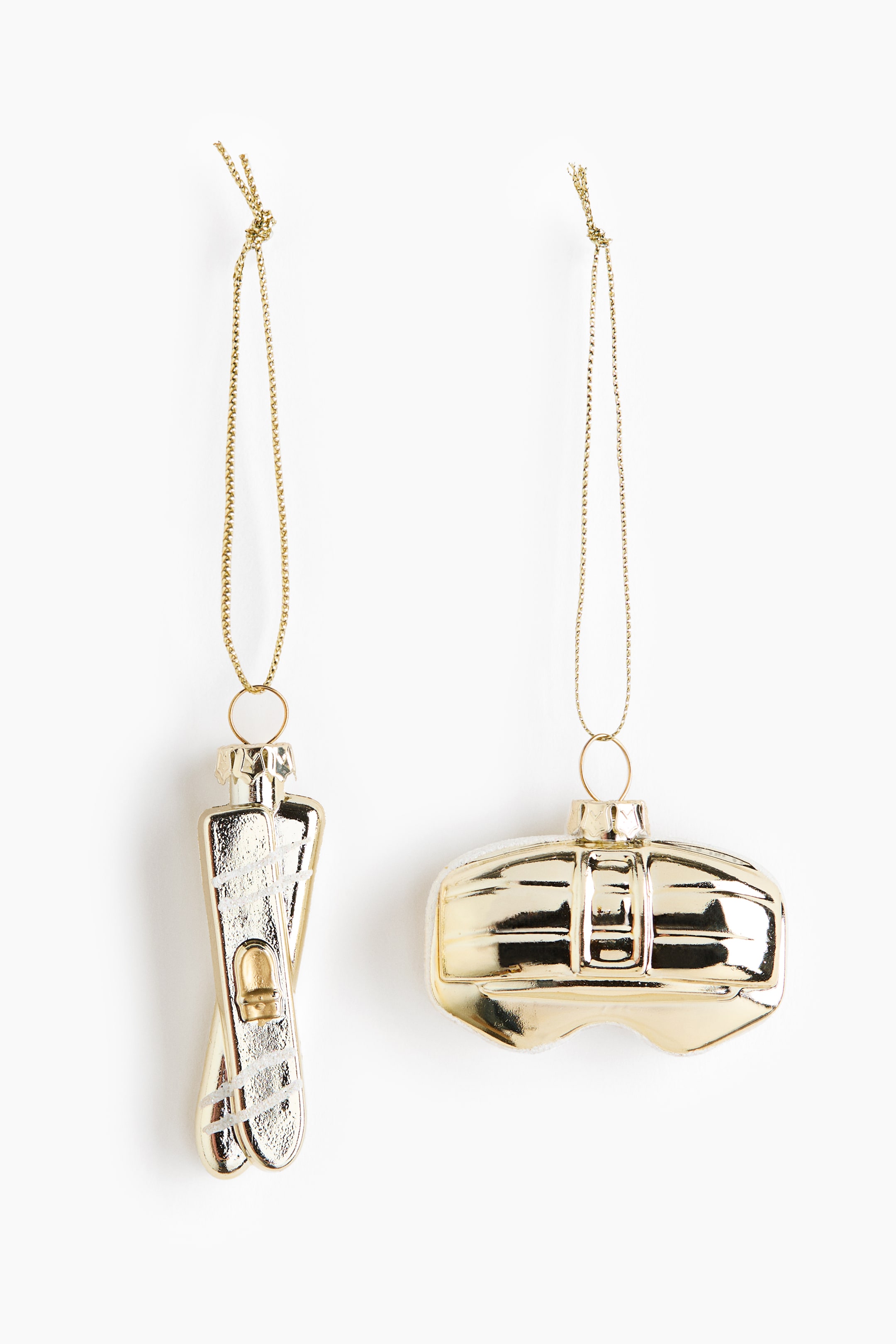 View larger image: Two gold-coloured ornaments are hanging from golden chains. The left ornament depicts a pair of crossed skis with white textured details, and the right ornament depicts a sports helmet with distinct ridges.