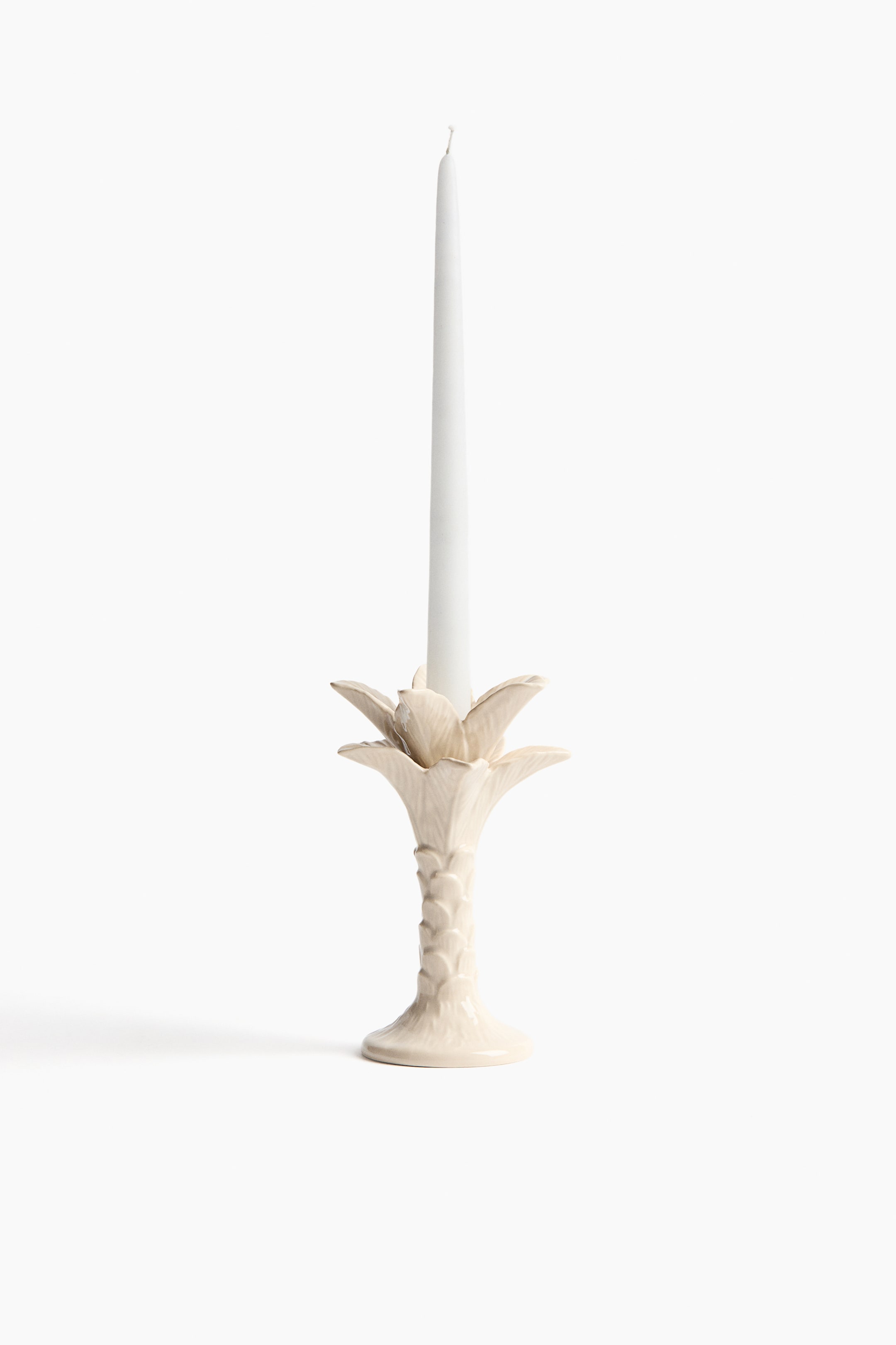 View larger image: A cream-colored candlestick holder, displayed front-facing, holds a white taper candle and features a palm tree design with a textured trunk-like stem and flared, frond-like details at its top.
