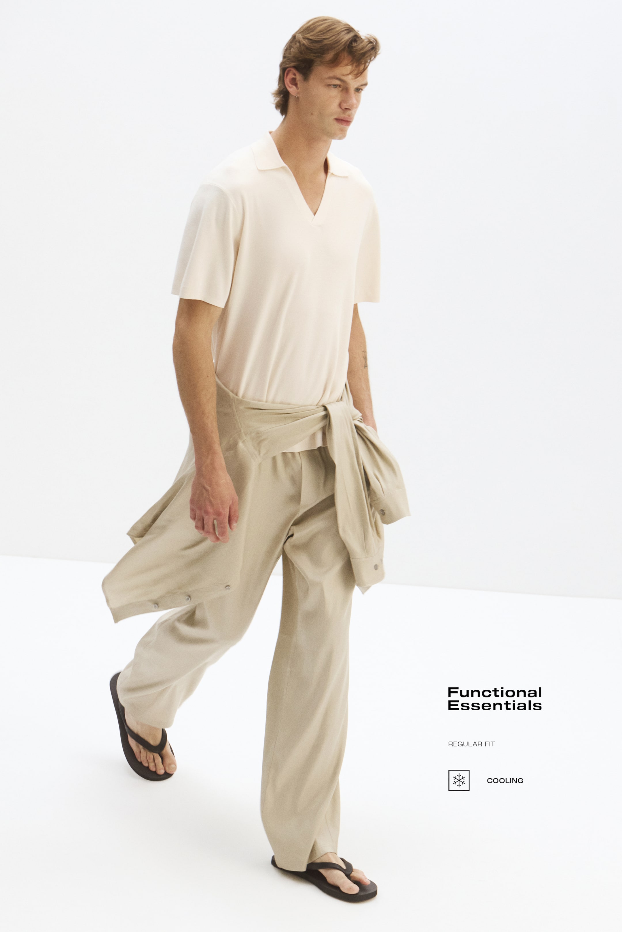Visualizza immagine più grande: Una polo color crema, caratterizzata da un colletto, apertura a V, maniche corte scese e una vestibilità regolare con orlo dritto, è indossata dalla modella e infilata in pantaloni a gamba larga di colore beige chiaro.