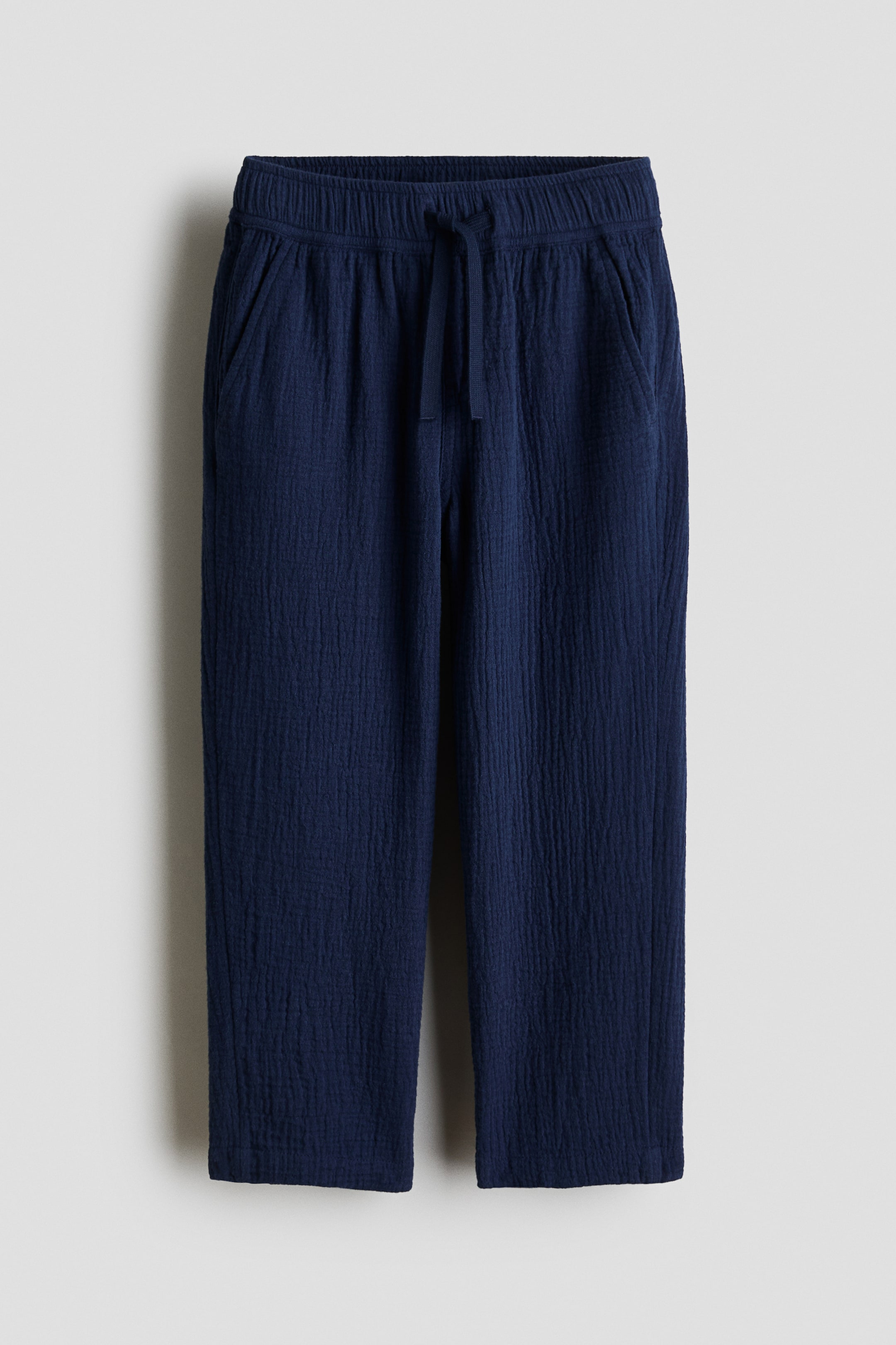 View larger image: Front-facing navy-blue pants featuring an elasticised waistband with a drawstring tie and two side pockets. A crinkled texture is visible throughout the fabric.