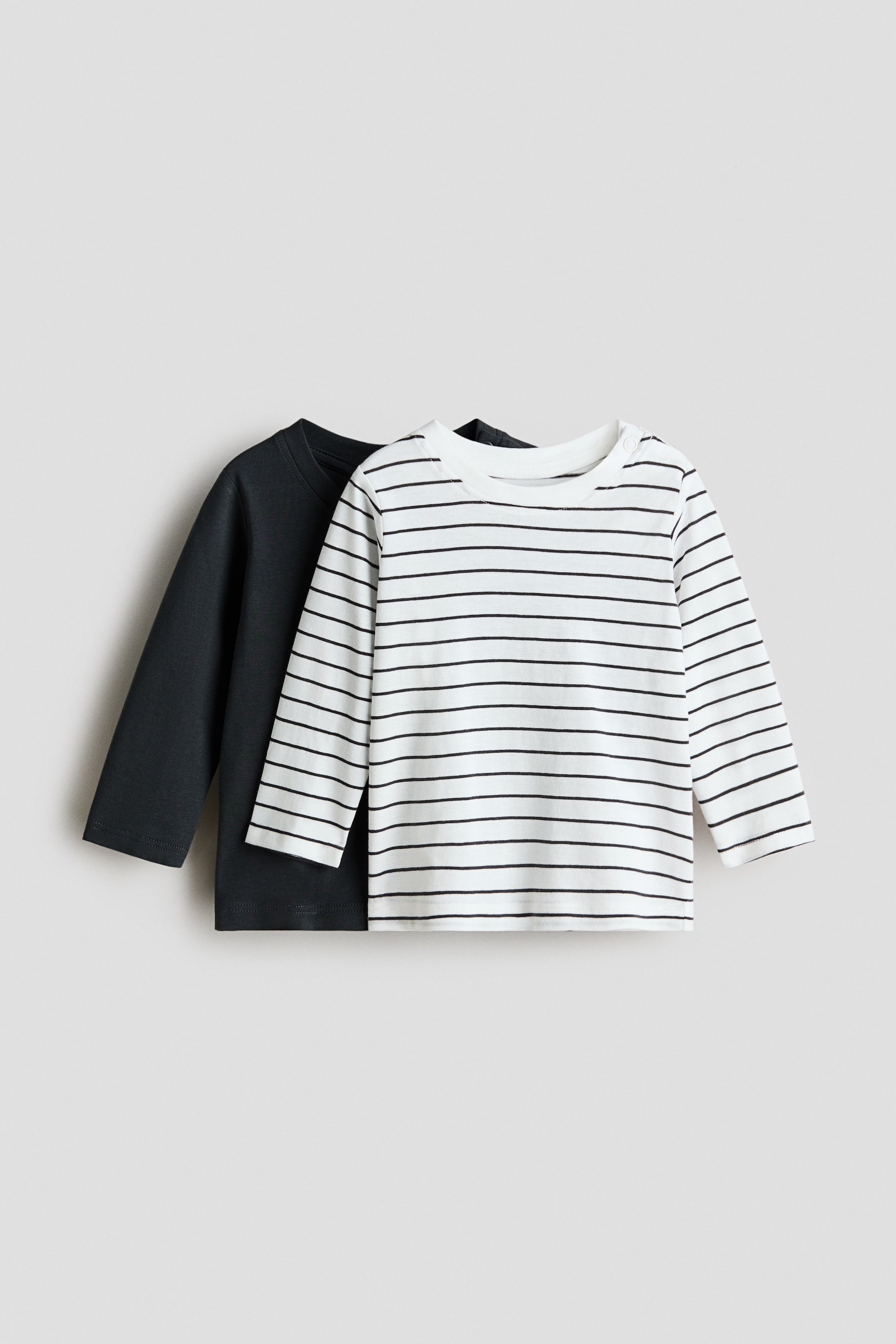 View larger image: A 2-pack of long-sleeved jersey tops is shown from the front, with the foreground top in white fabric featuring black horizontal stripes, a round-neck and shoulder snap buttons, and the background top in a solid dark grey.