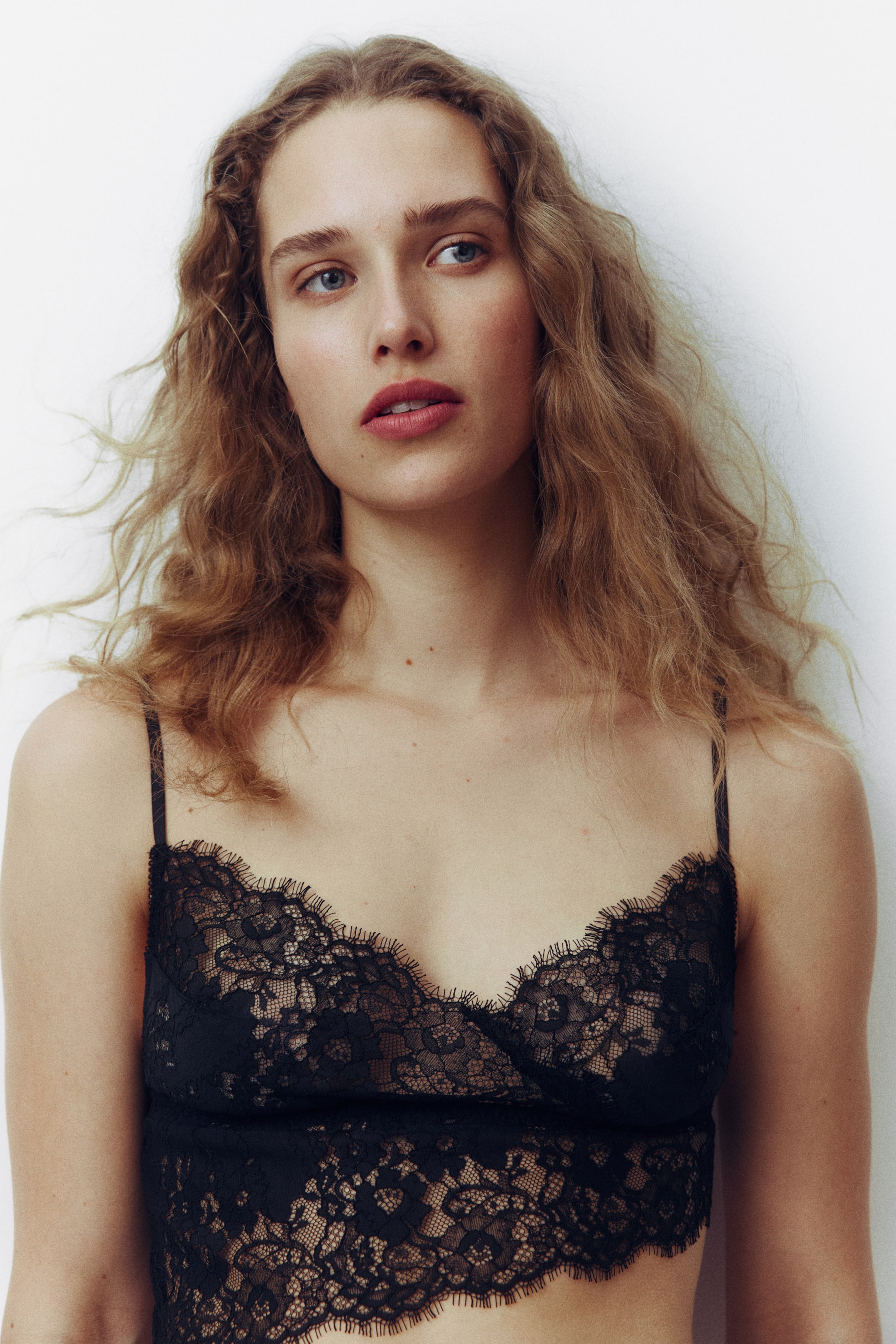 Größeres Bild ansehen: Ein schwarzes Spitzen-Bralette mit dünnen Spaghettiträgern und einem V-Ausschnitt mit Muschelkante, das ein filigranes florales Spitzenmuster mit einem muschelförmigen Saum präsentiert.