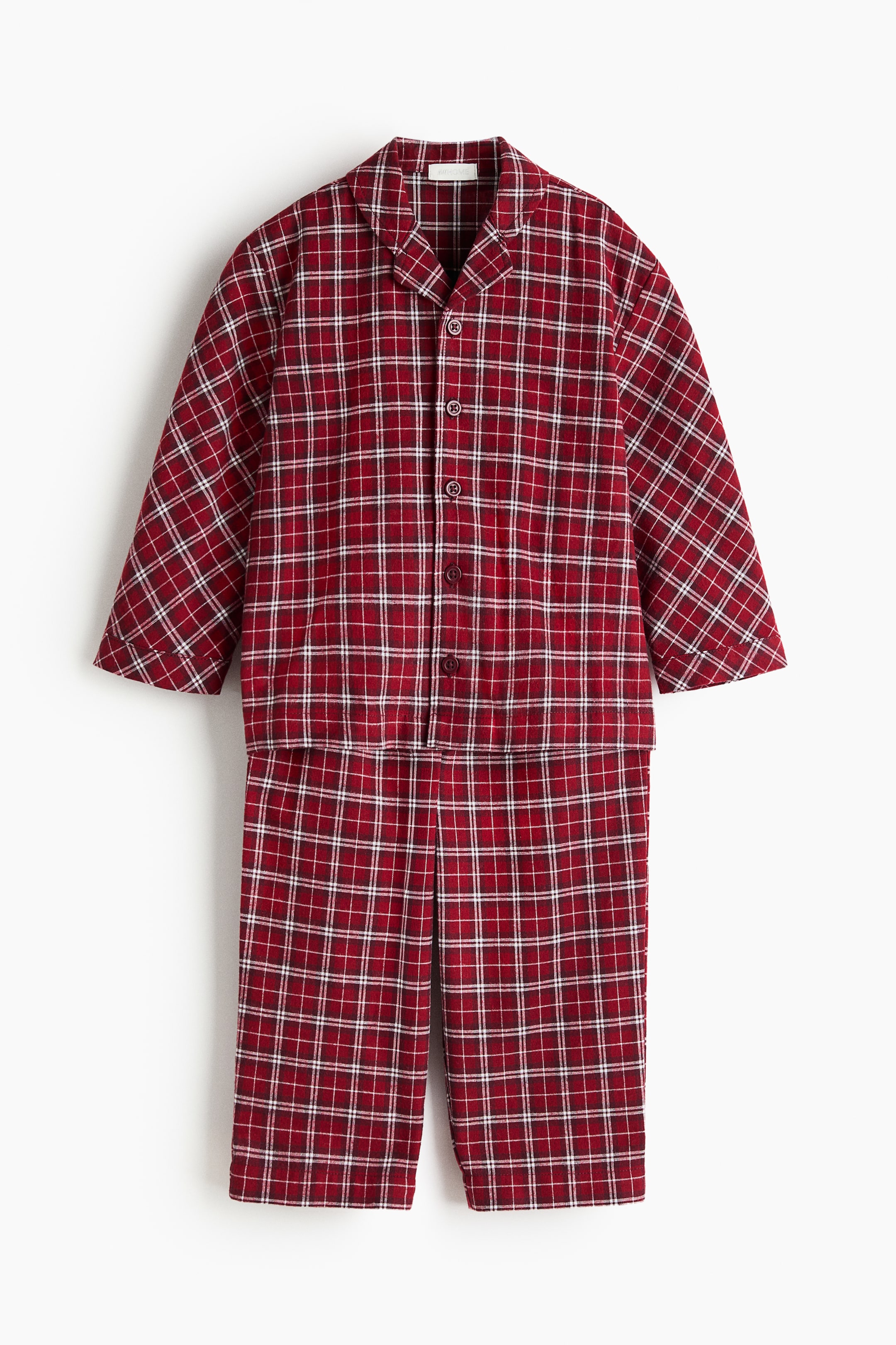 Grotere afbeelding bekijken: Een tweedelige pyjamaset wordt van voren getoond, met een bijpassende top met lange mouwen en een rechte broek in een geruit patroon in rood, wit en zwart. De knoopsluiting op de top toont revers met inkeping en donkere knopen, terwijl de bijpassende broek eronder hangt om de set compleet te maken.