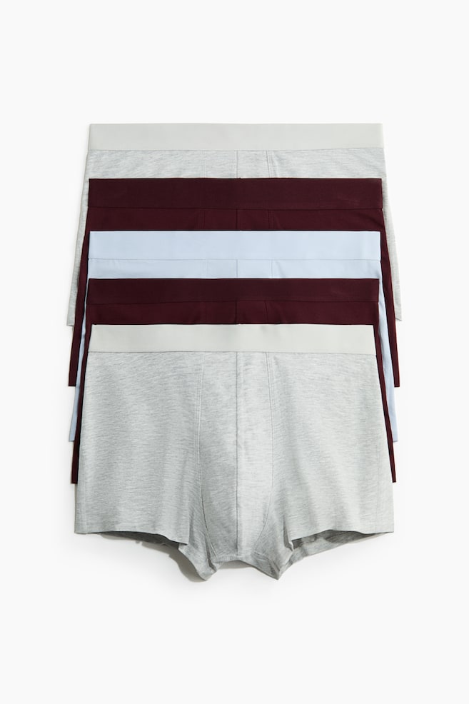 Um conjunto de cinco boxers masculinos está disposto de forma plana, exibindo os seus painéis frontais. Os pares superior e inferior são cinza mesclado claro com um cós elástico cinza mais claro, enquanto os três pares do meio alternam entre vermelho escuro e azul claro, cada um com um cós elástico a condizer. - 1