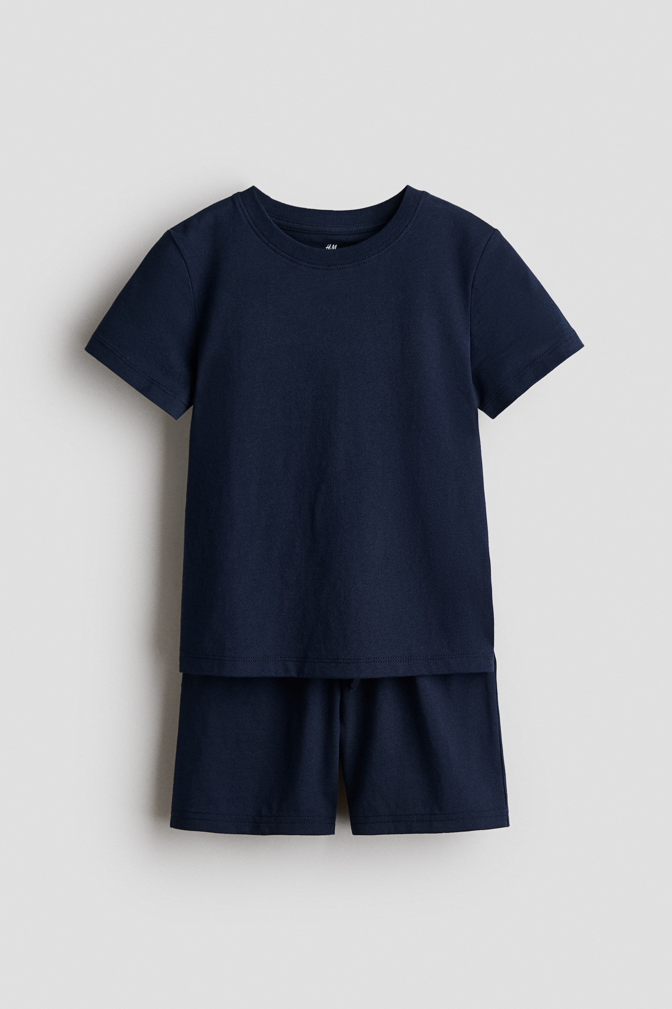 Visualizza immagine più grande: Un set composto da una maglietta e pantaloncini blu navy è in mostra, con la maglietta che presenta uno scollo rotondo rifinito a coste, maniche corte e un orlo a taglio dritto. I pantaloncini sono progettati con una vita elasticizzata e un cordoncino regolabile.