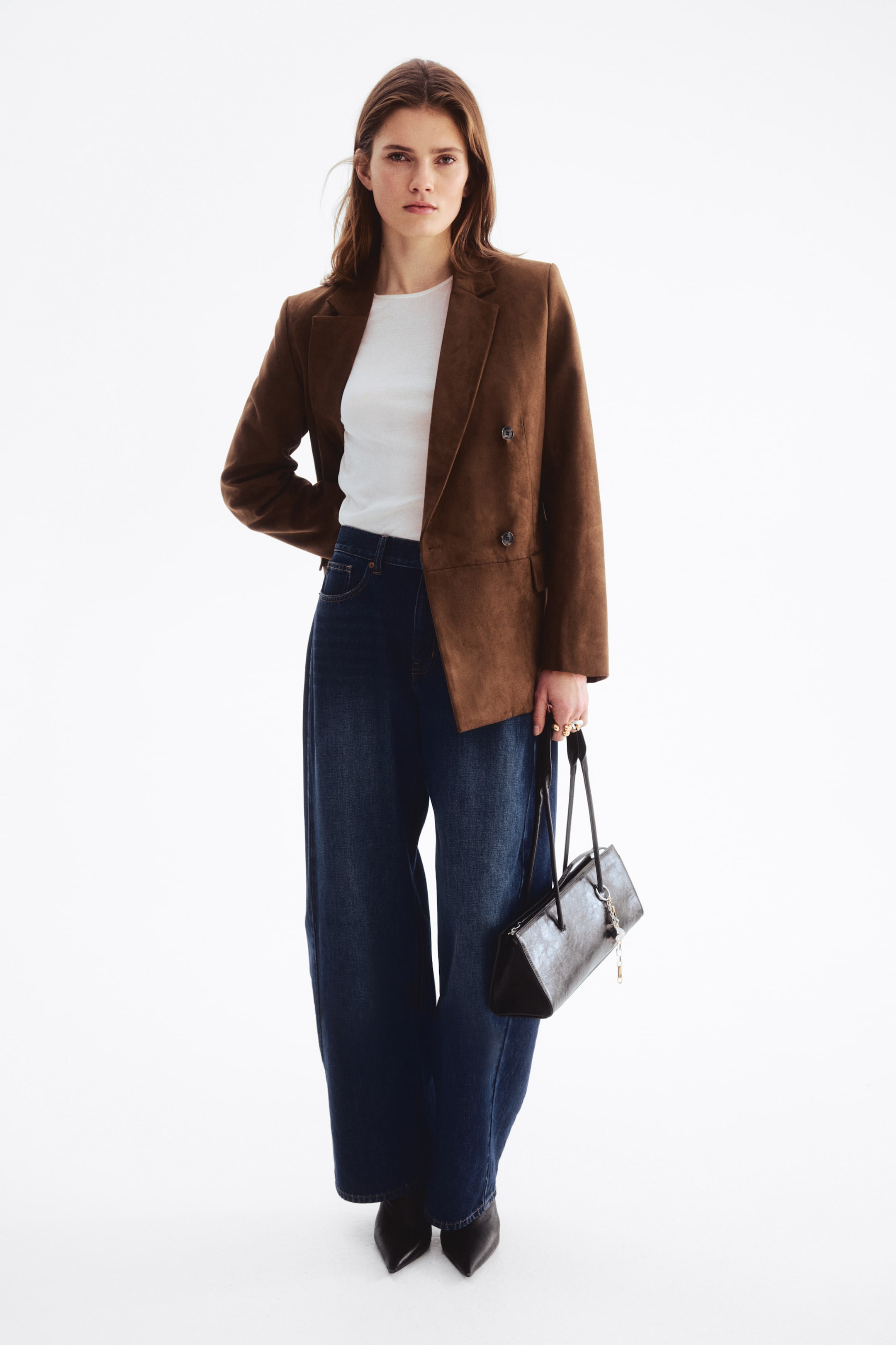 Größeres Bild anzeigen: Ein brauner, zweireihiger Blazer aus gewebtem Stoff mit weichem, aufgerautem Finish wird vom Model getragen. Er verfügt über Kerbrevers, Schulterpolster, Pattentaschen vorne und ist gefüttert. Der Blazer wird über einem weißen Oberteil und dunkelblauen, weit geschnittenen Jeans gestylt.