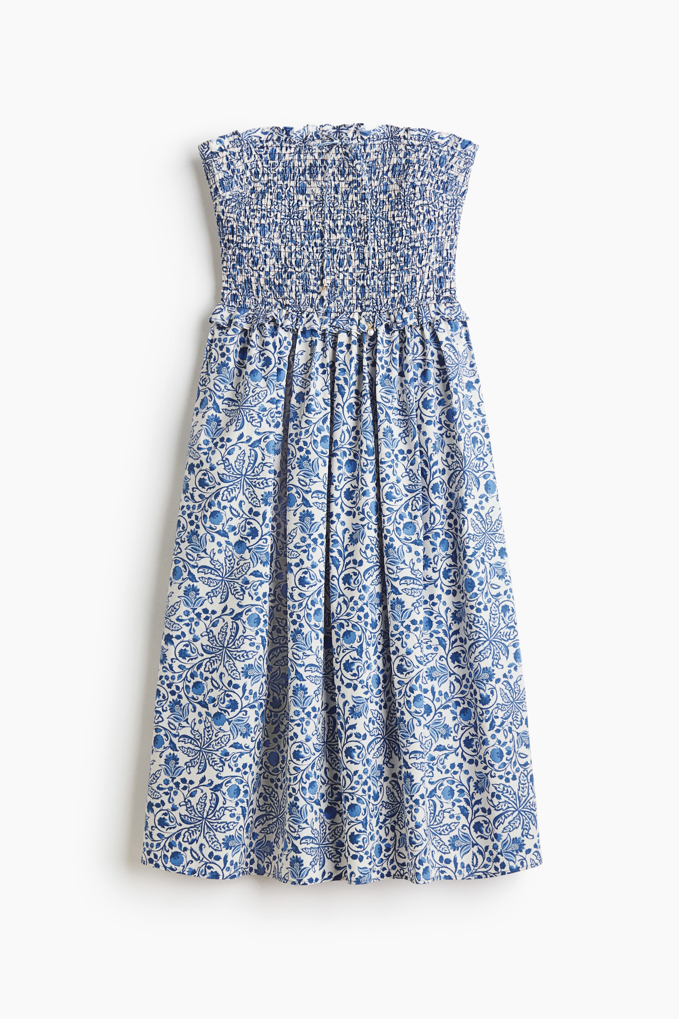 View larger image: This strapless dress showcases a smocked bodice paired with a flowing skirt, adorned in a blue and white botanical motif. The skirt gathers gracefully below the smocked waist, offering an elegant silhouette.